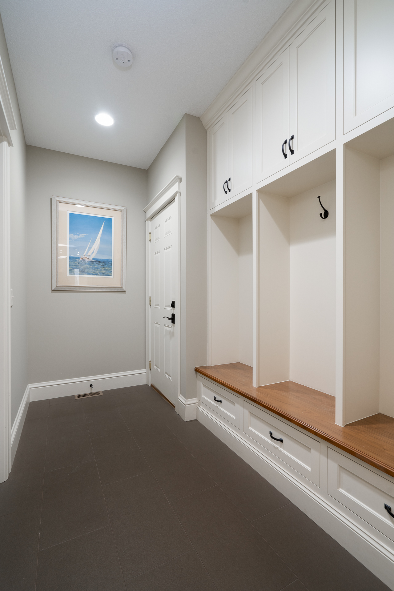 A stylish and functional mudroom featuring white cabinetry and a nautical painting.