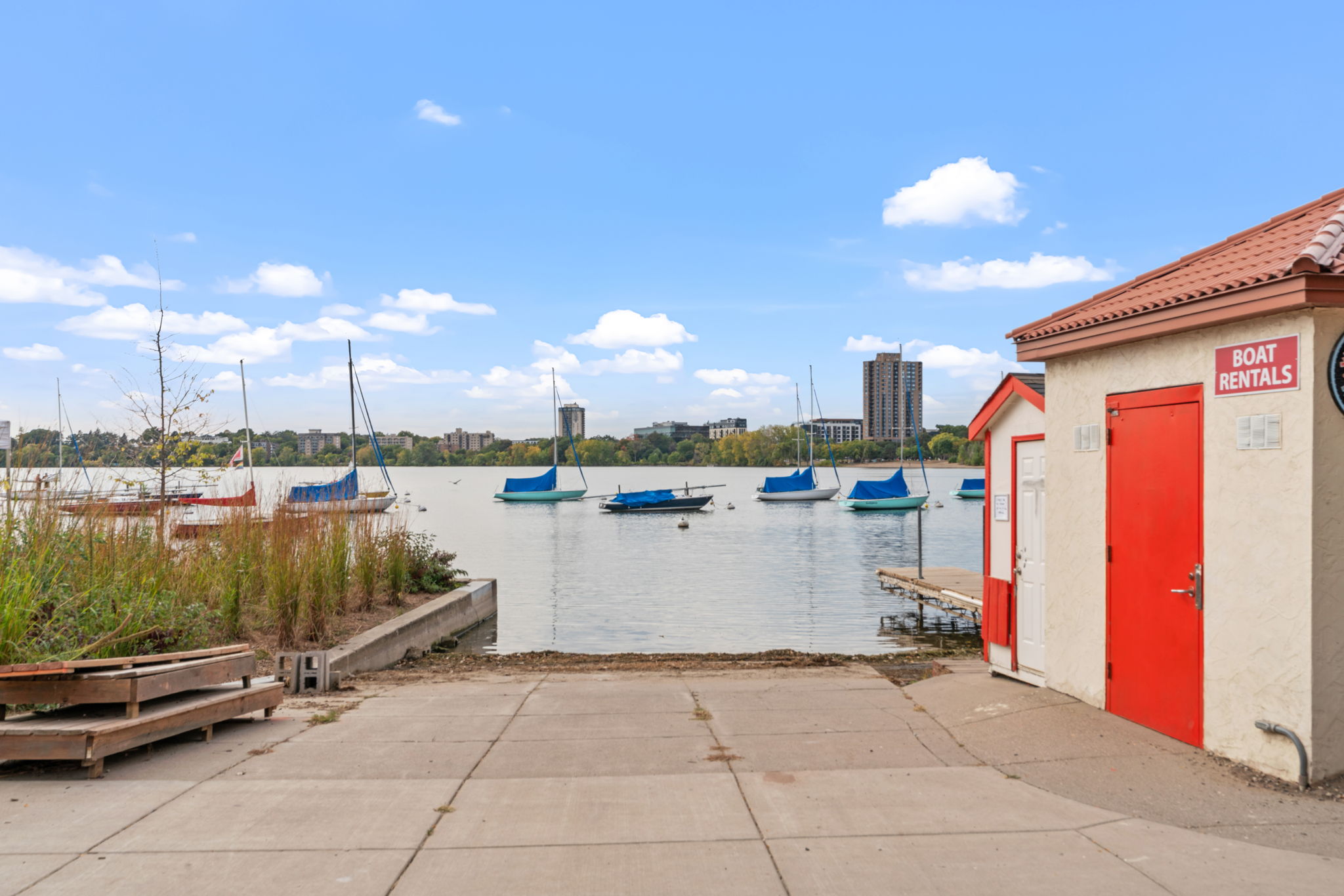 A picturesque lakeside with sailboats and a boat rental shack.