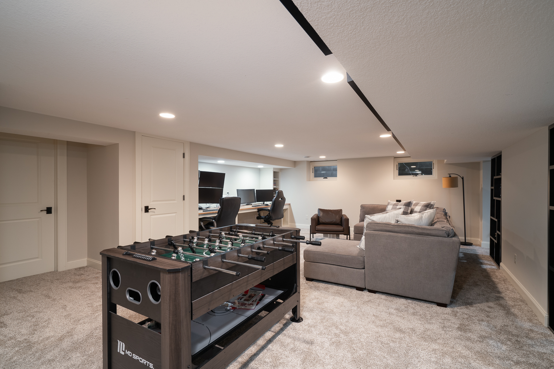 A stylish and functional basement living area featuring a foosball table, cozy seating, and a work space.