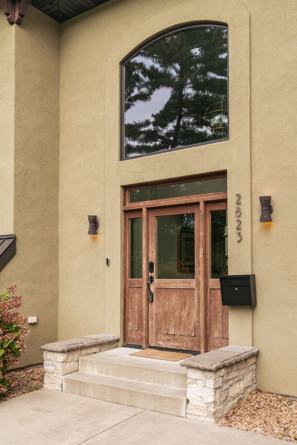 A modern home entrance featuring wooden double doors and a large arched window.