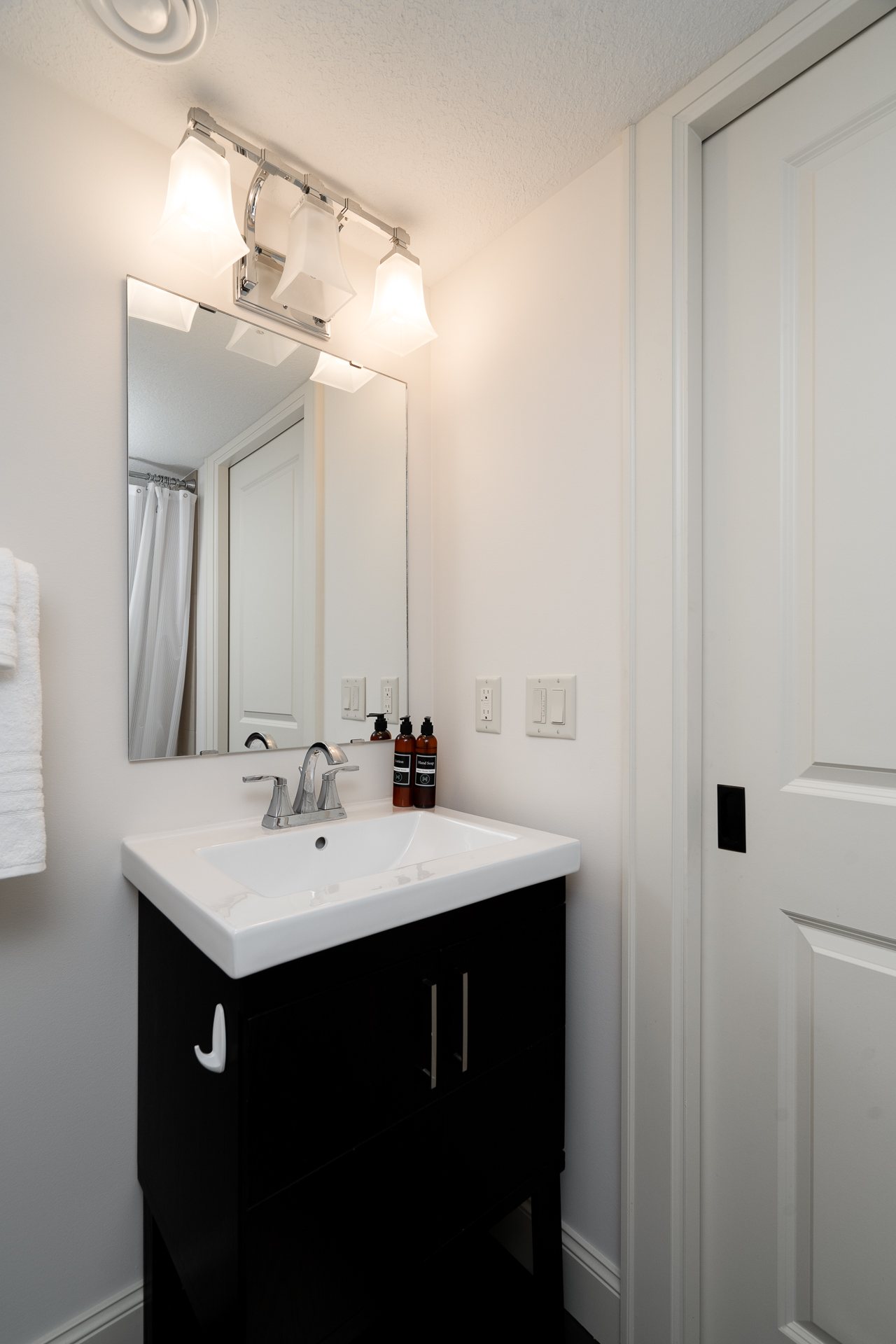 A modern bathroom with a black vanity, illuminated mirrors, and a cozy ambiance.