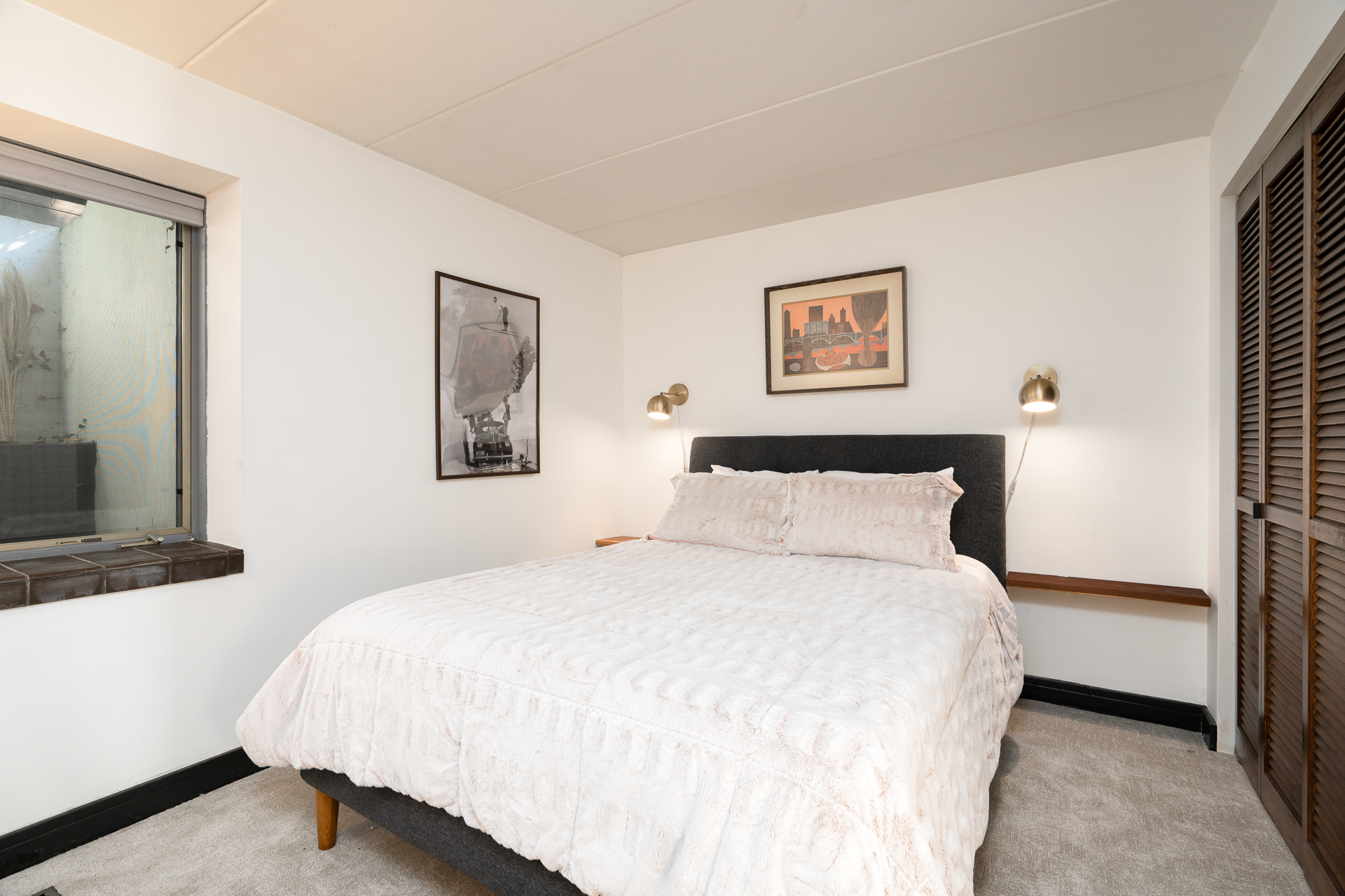 A cozy and minimalistic bedroom with textured bedding and framed artworks.