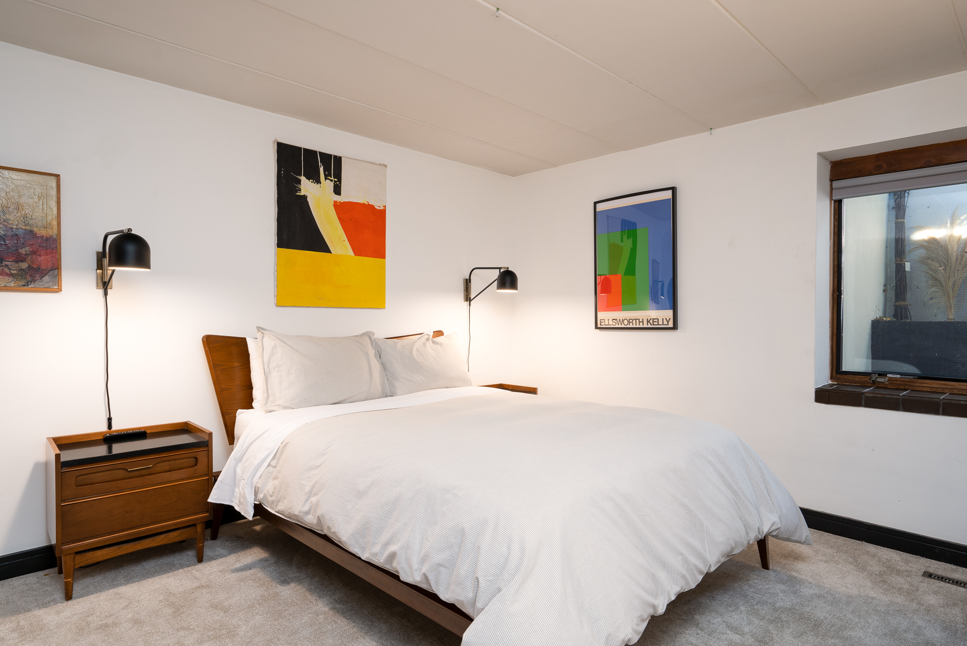A cozy, modern bedroom featuring minimalist decor and vibrant artwork.