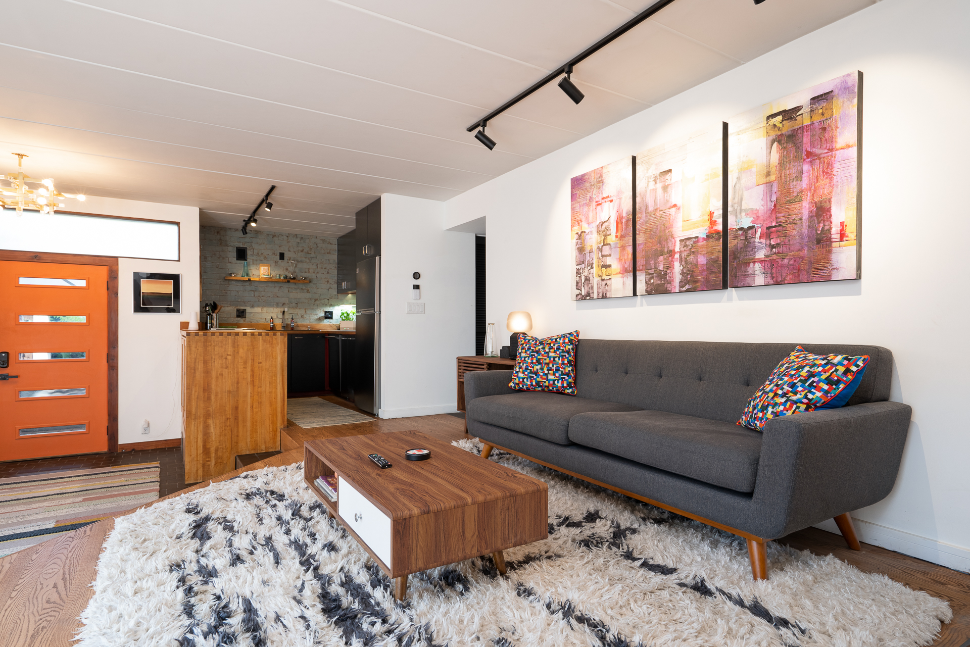 A modern living space with a stylish gray sofa, colorful accents, and a sleek kitchen.