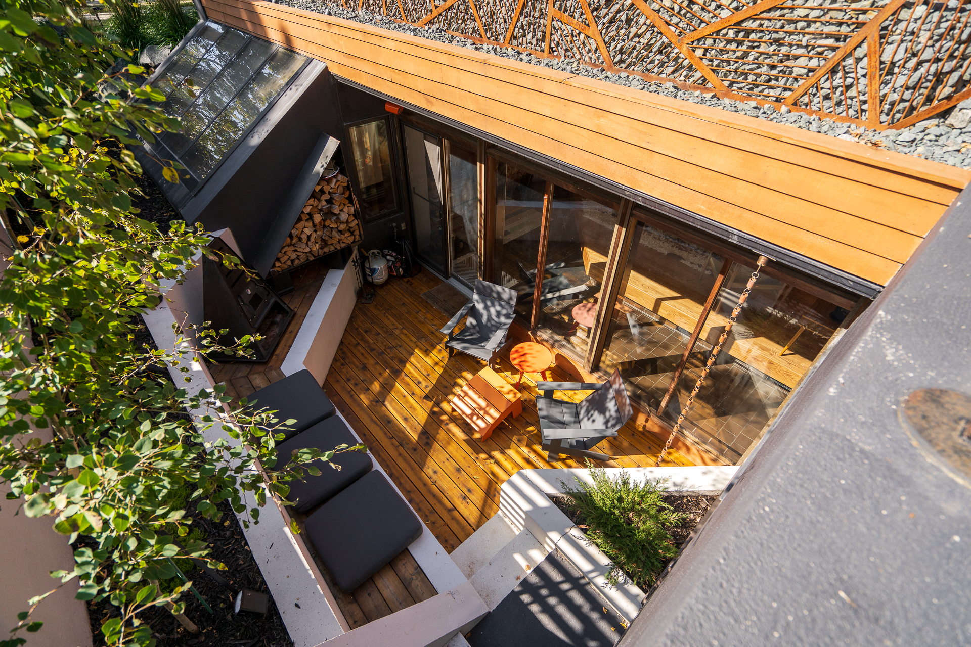 An aerial view of a stylish outdoor space featuring wooden decking, modern furniture, and a slanted glass roof.