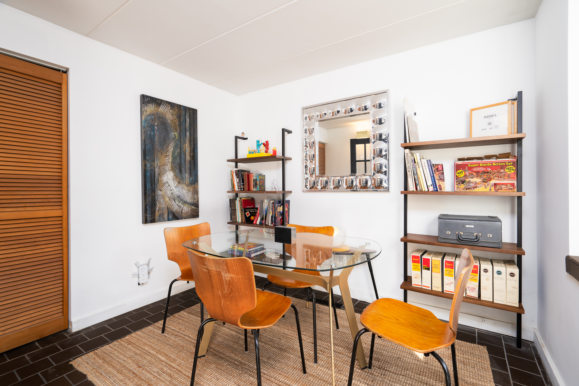 A modern dining area featuring a glass table, mid-century chairs, and a vibrant art piece.