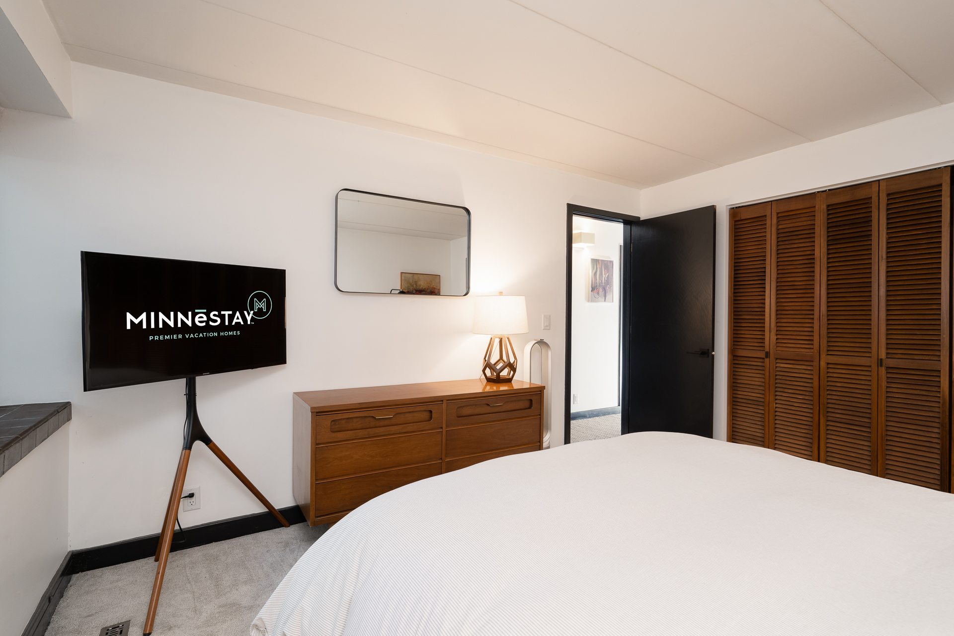 A modern and inviting bedroom featuring a TV, dresser, and warm lighting.