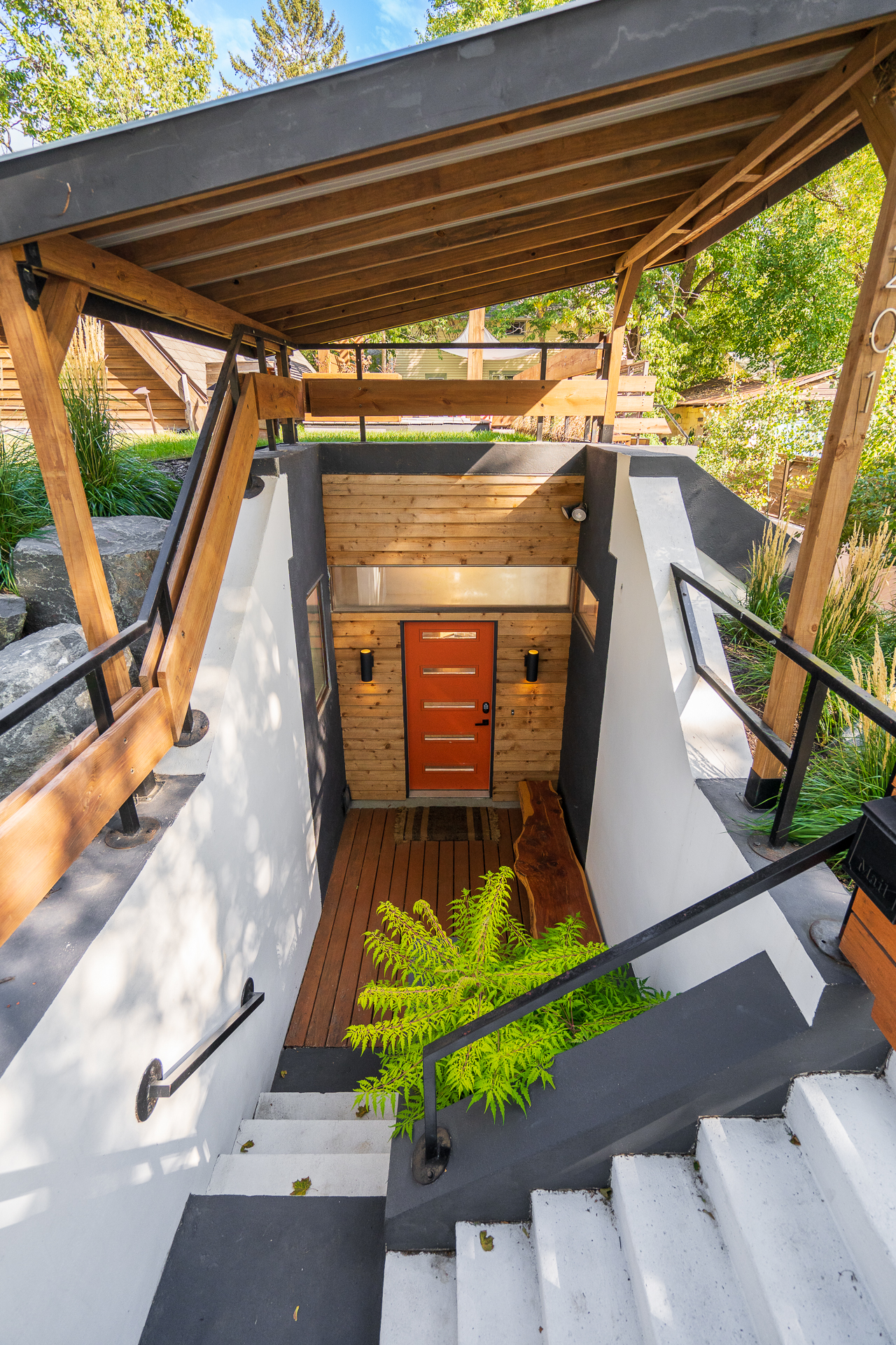 A modern entrance with a vibrant orange door and lush greenery.