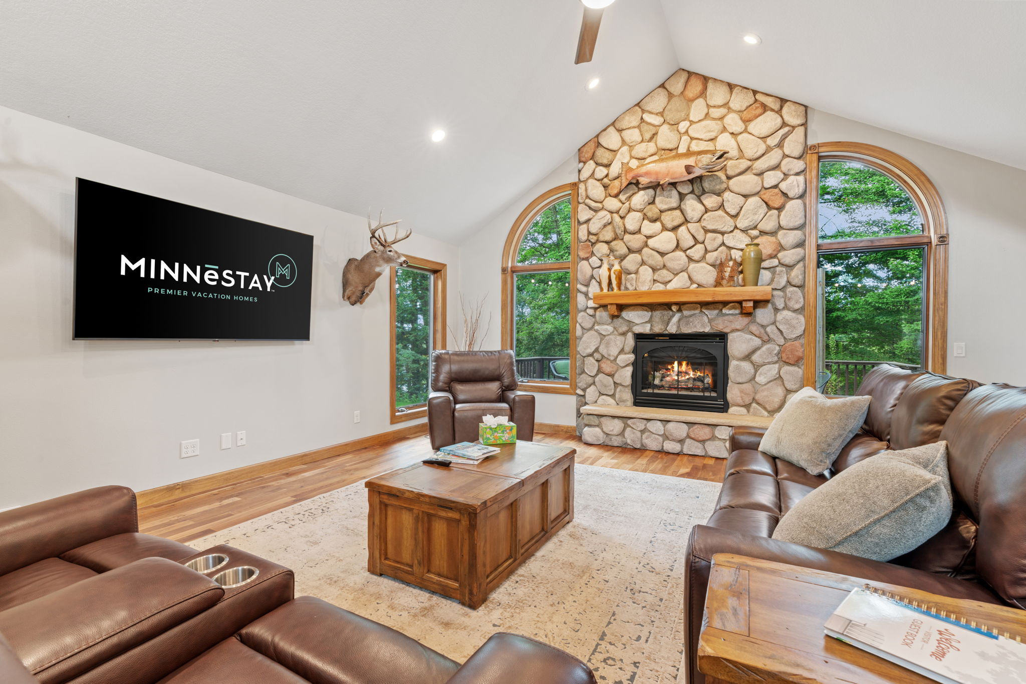 Cozy living room featuring leather sofas, a stone fireplace, and large windows.