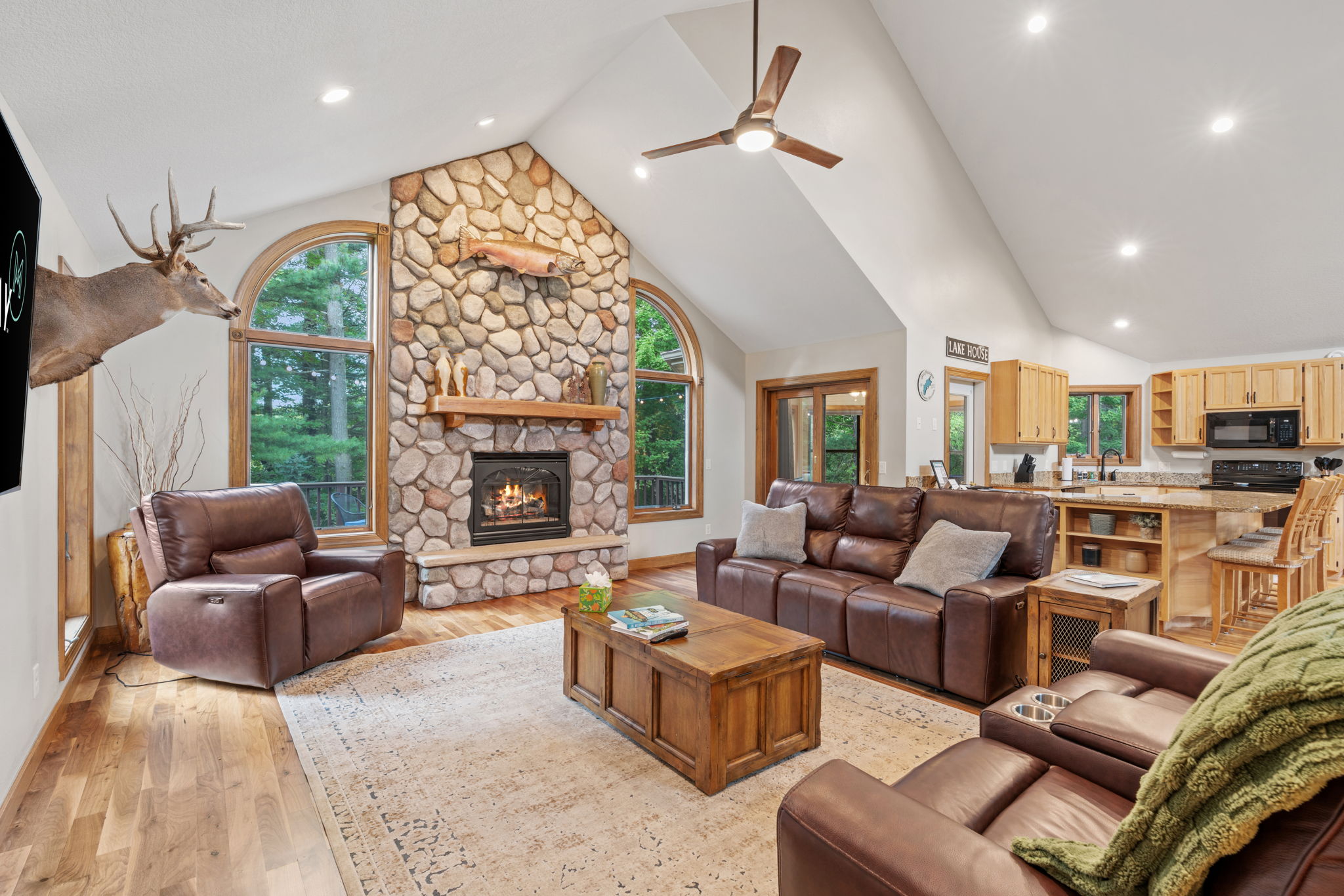 A cozy living room featuring a stone fireplace, leather sofas, and natural lighting.