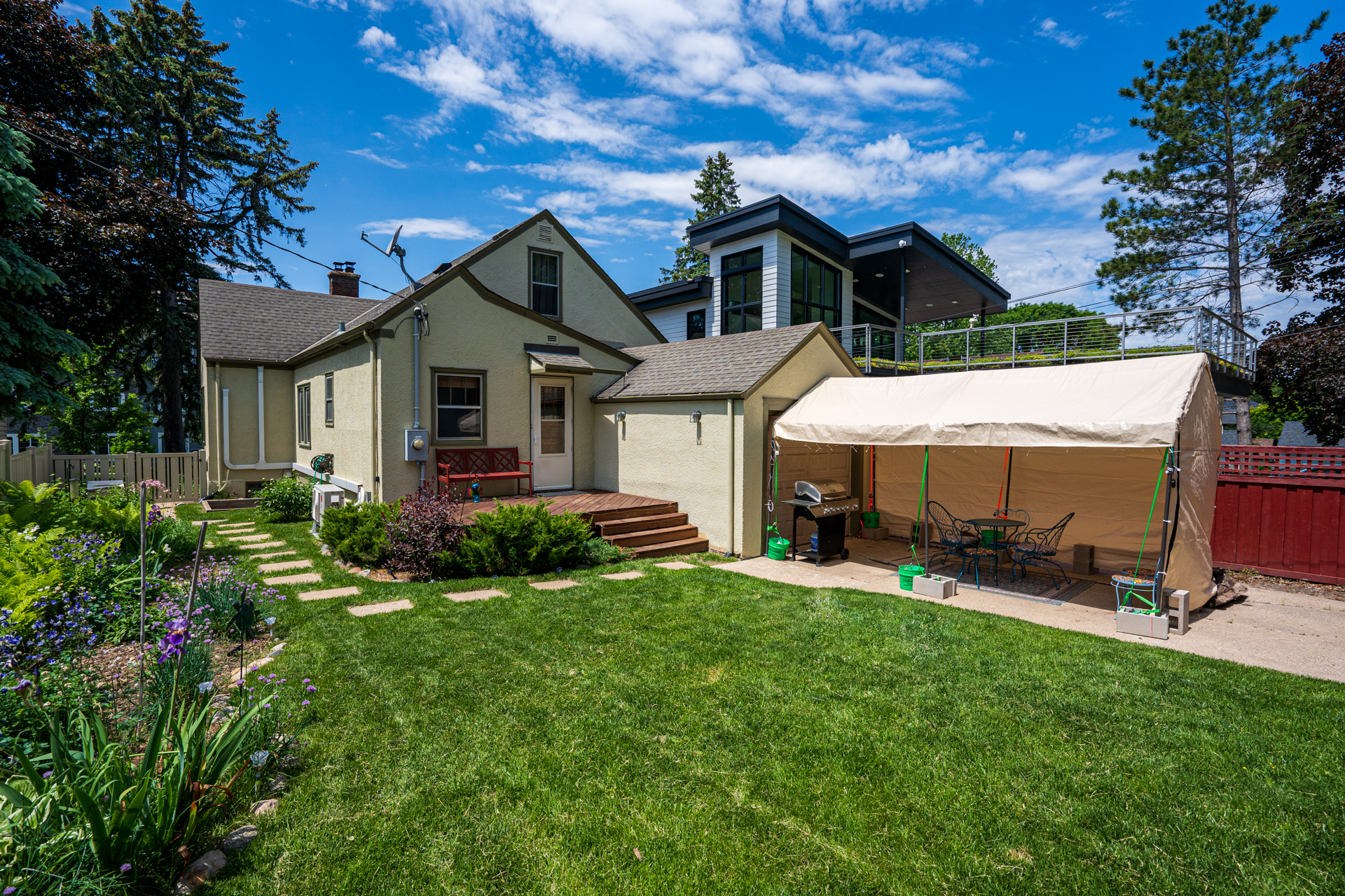 A beautiful backyard featuring a charming house, modern extension, and a cozy dining area under a tent.