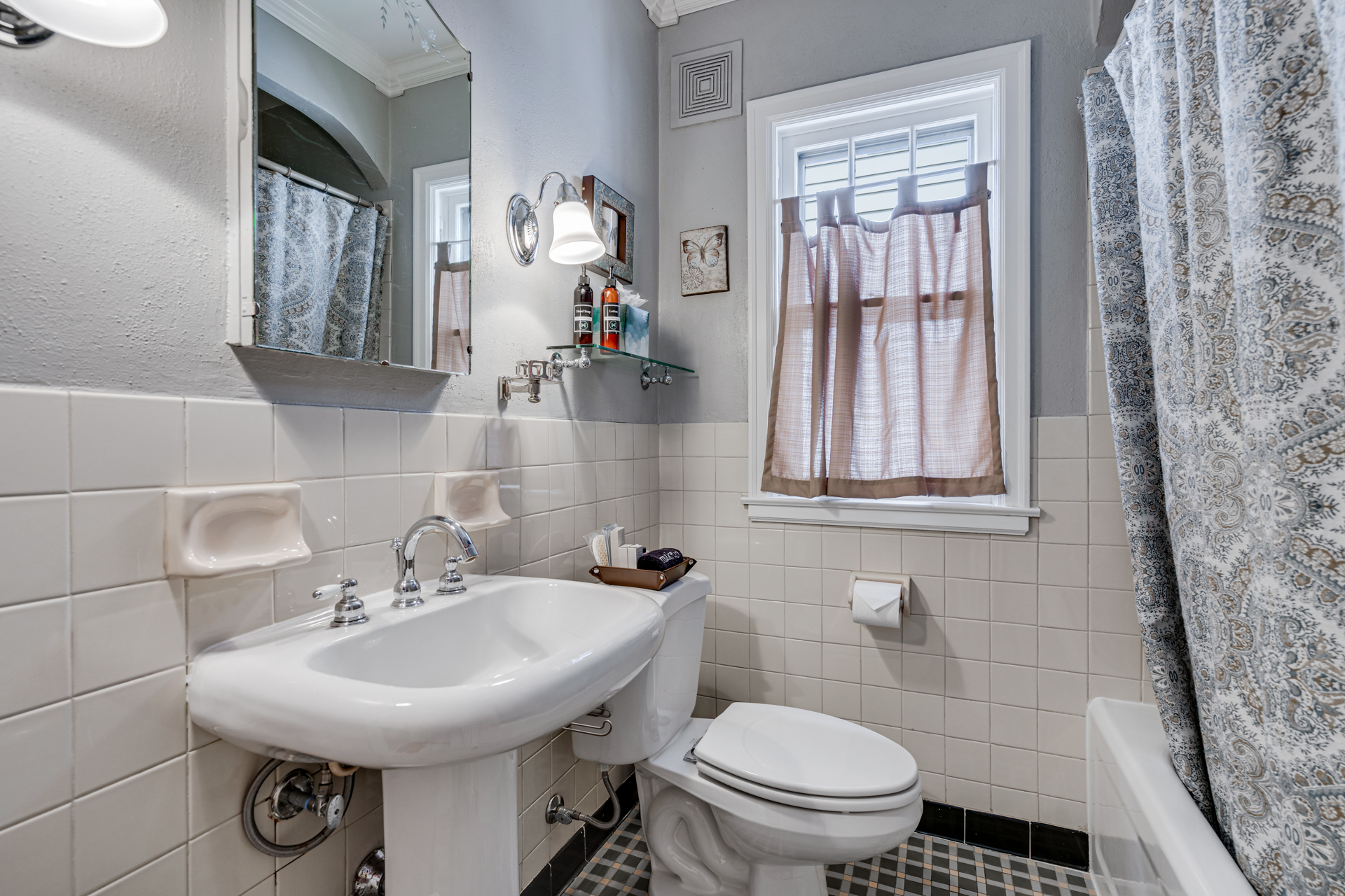 A cozy and stylish bathroom featuring a pedestal sink, decorative elements, and inviting lighting.