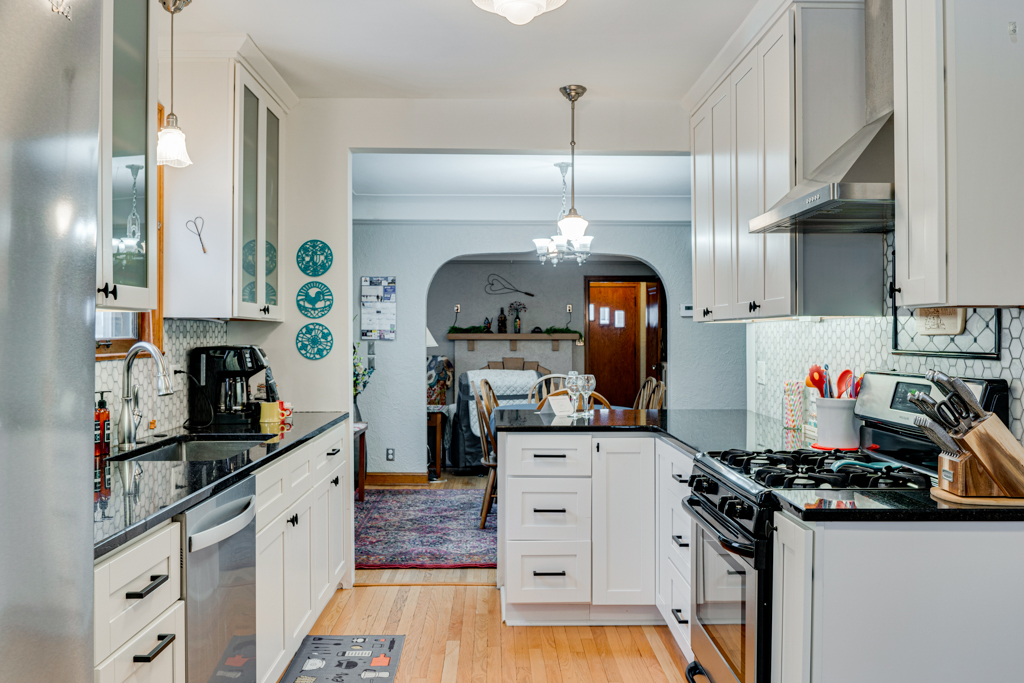 A modern kitchen featuring an open layout with white cabinetry and polished black countertops.