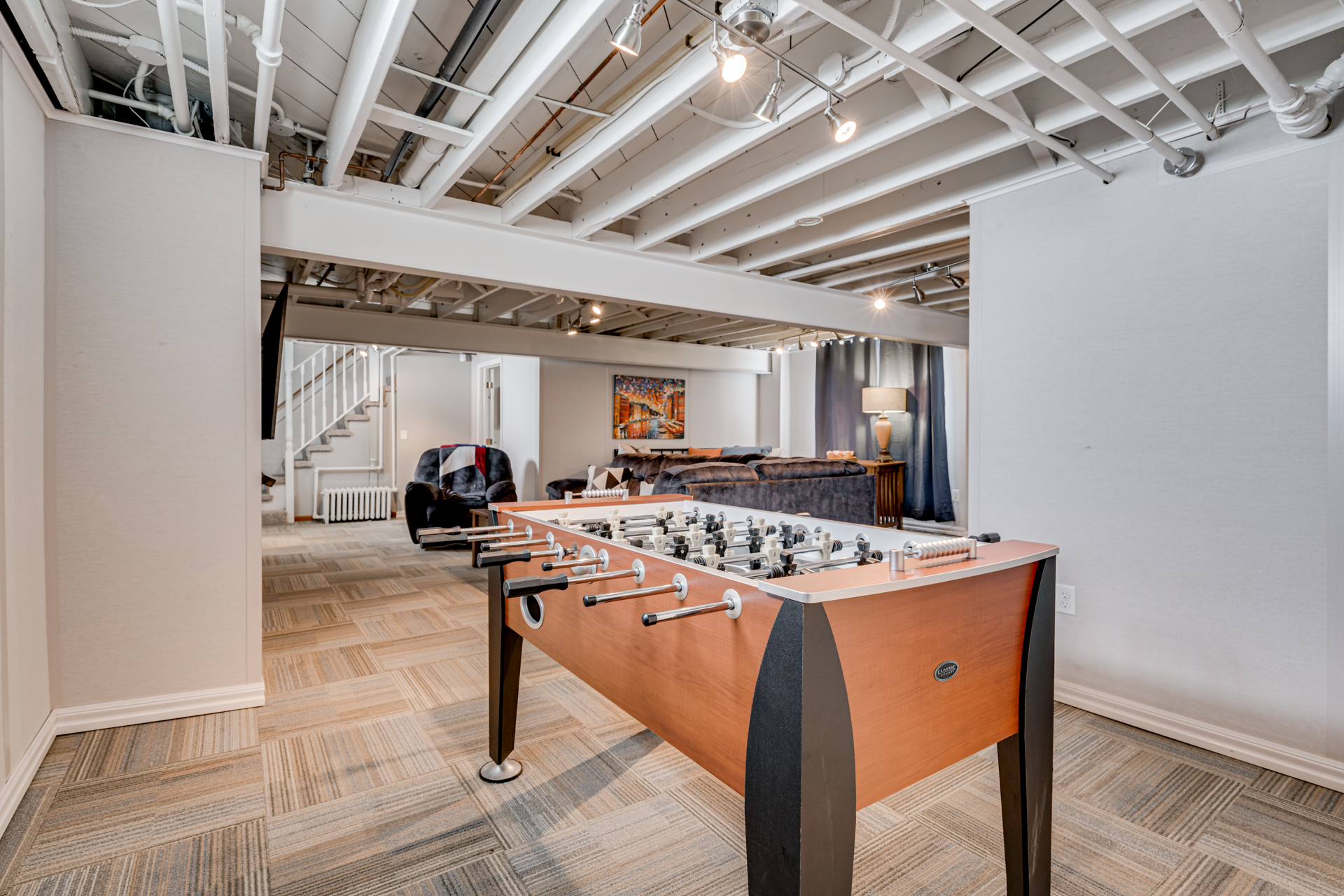 A stylish basement game room featuring a foosball table and a cozy seating area.