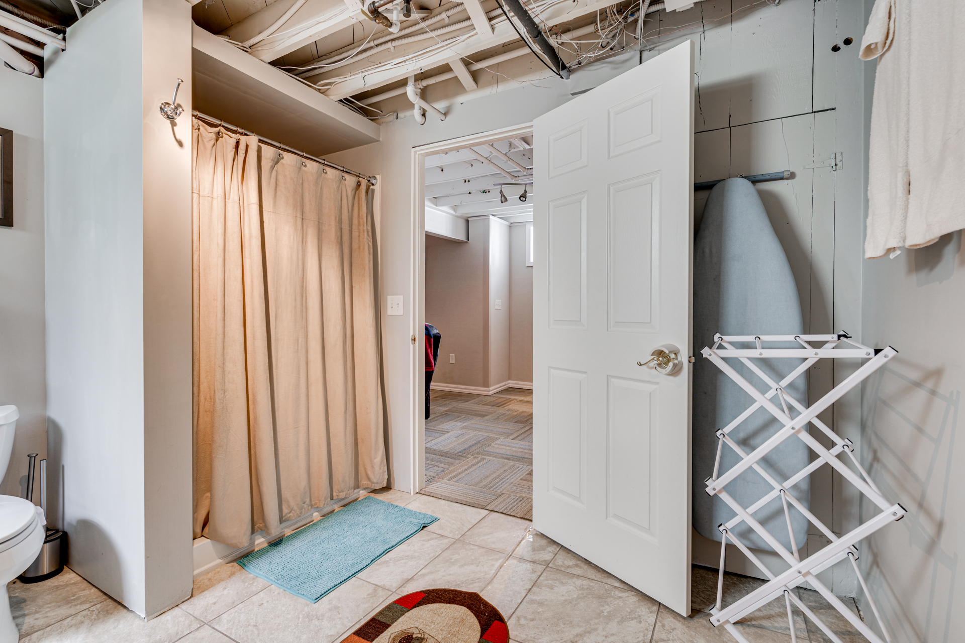 A functional bathroom featuring a shower, toilet, and ironing board.