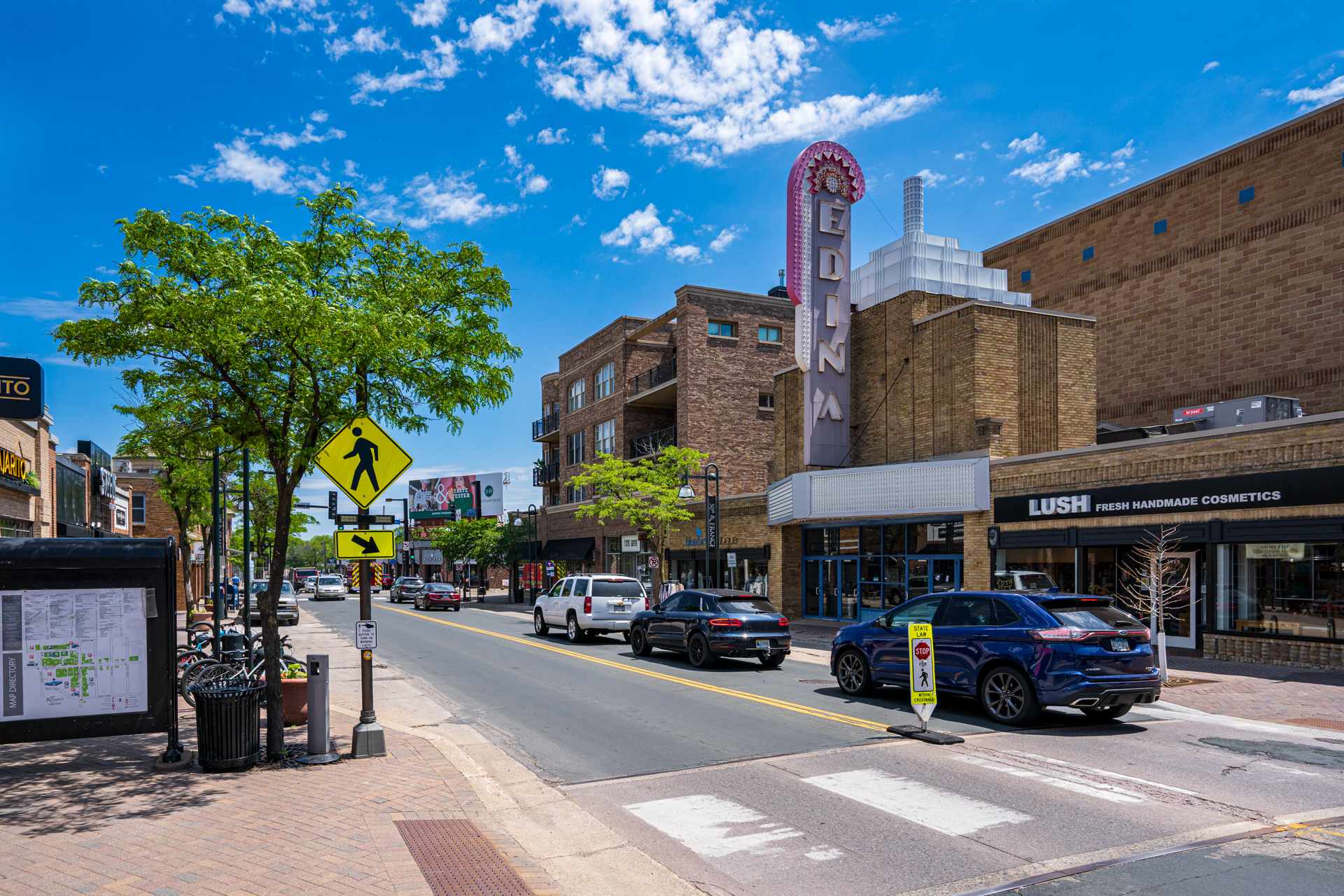 A bustling street scene in Edina featuring shops, cars, and a clear blue sky.