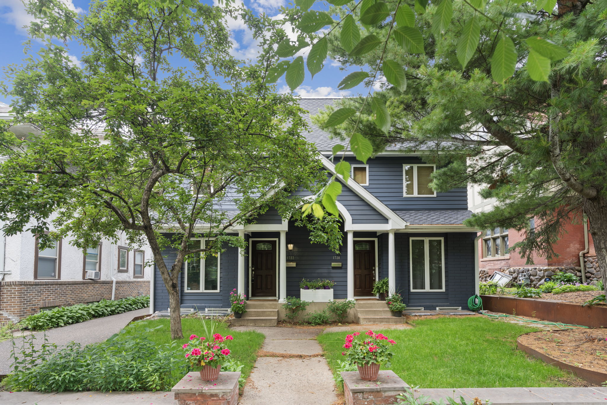 A blue duplex with flower pots and trees in front of it, under a blue sky.