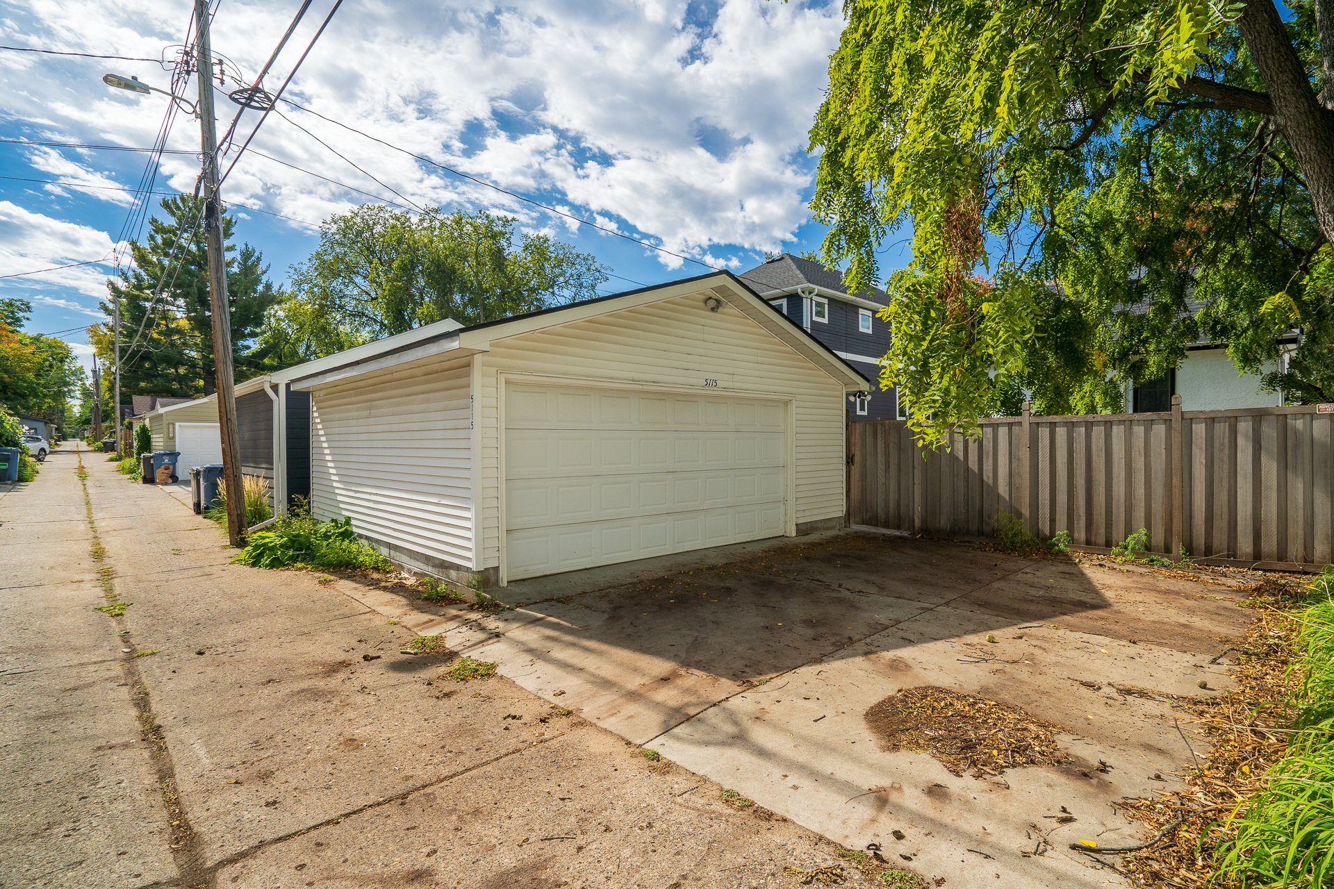 A serene alleyway featuring a white garage and lush greenery.