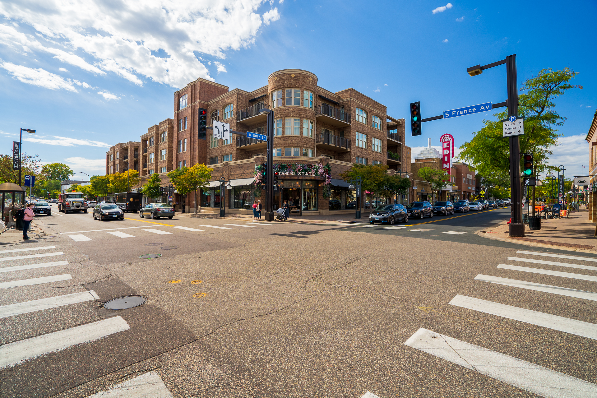 A lively urban intersection featuring a mix of vehicles, pedestrians, and shops.