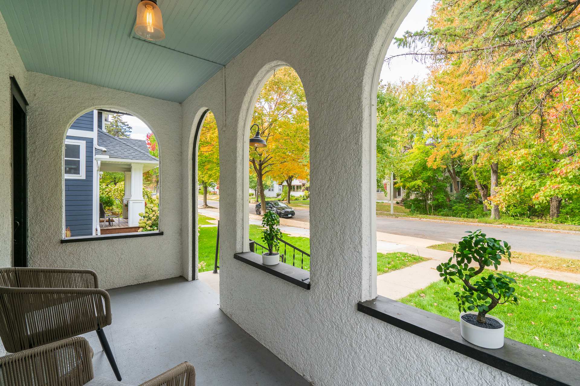 A cozy and inviting porch with arches overlooking a vibrant tree-lined street.