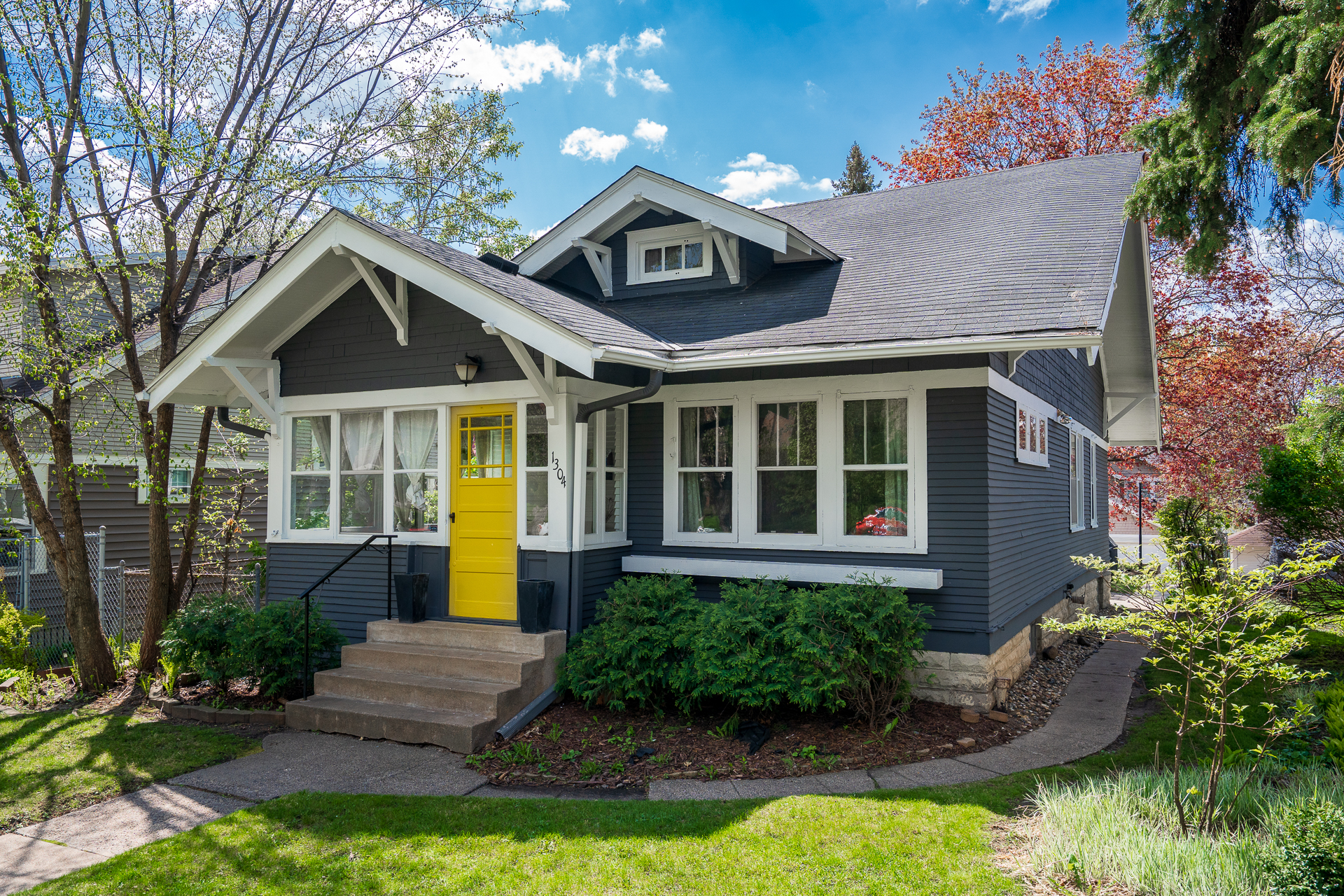 Charming gray house with a bright yellow door and lush landscaping.