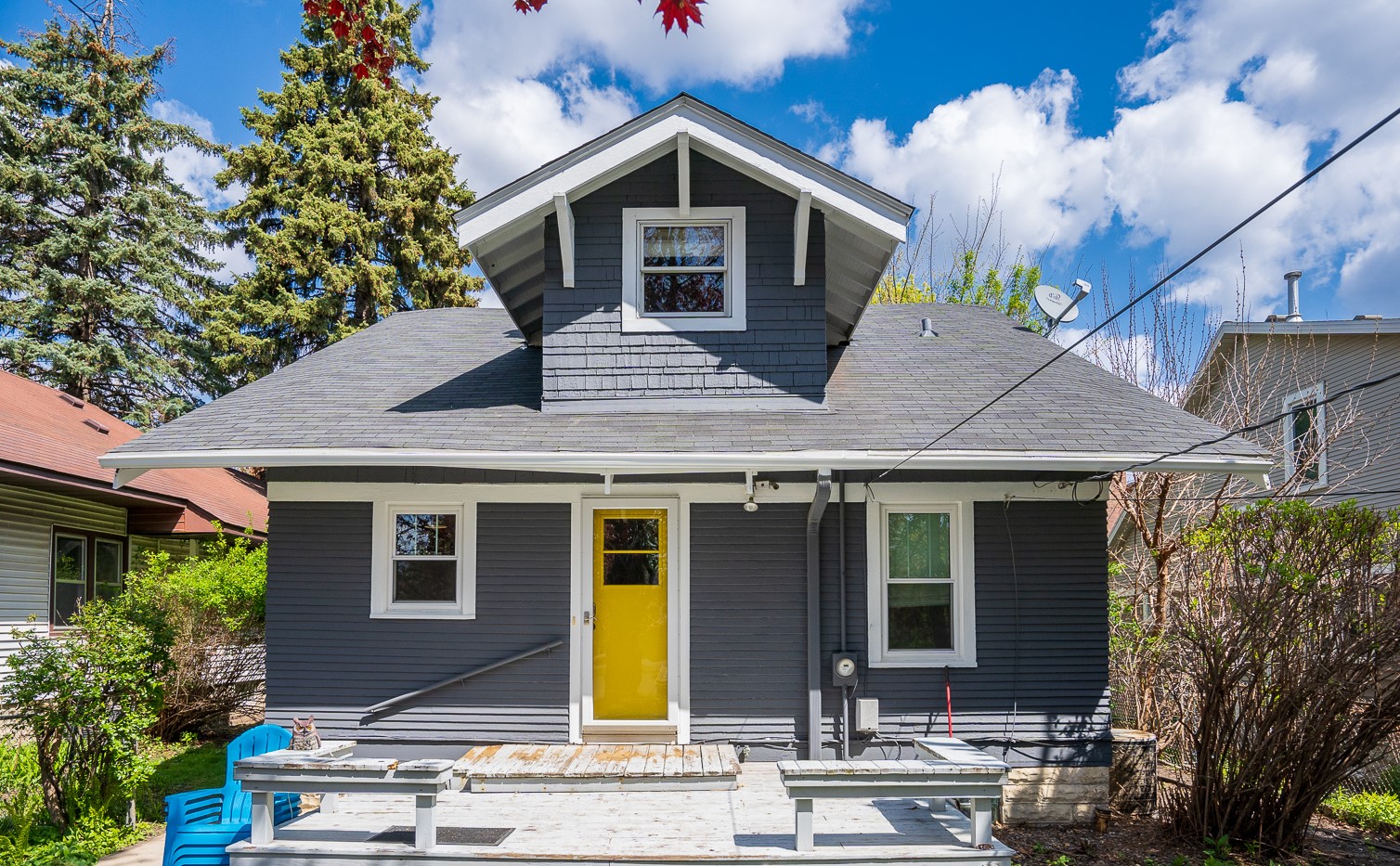 A charming gray house with a bright yellow door and blue chairs on the porch.