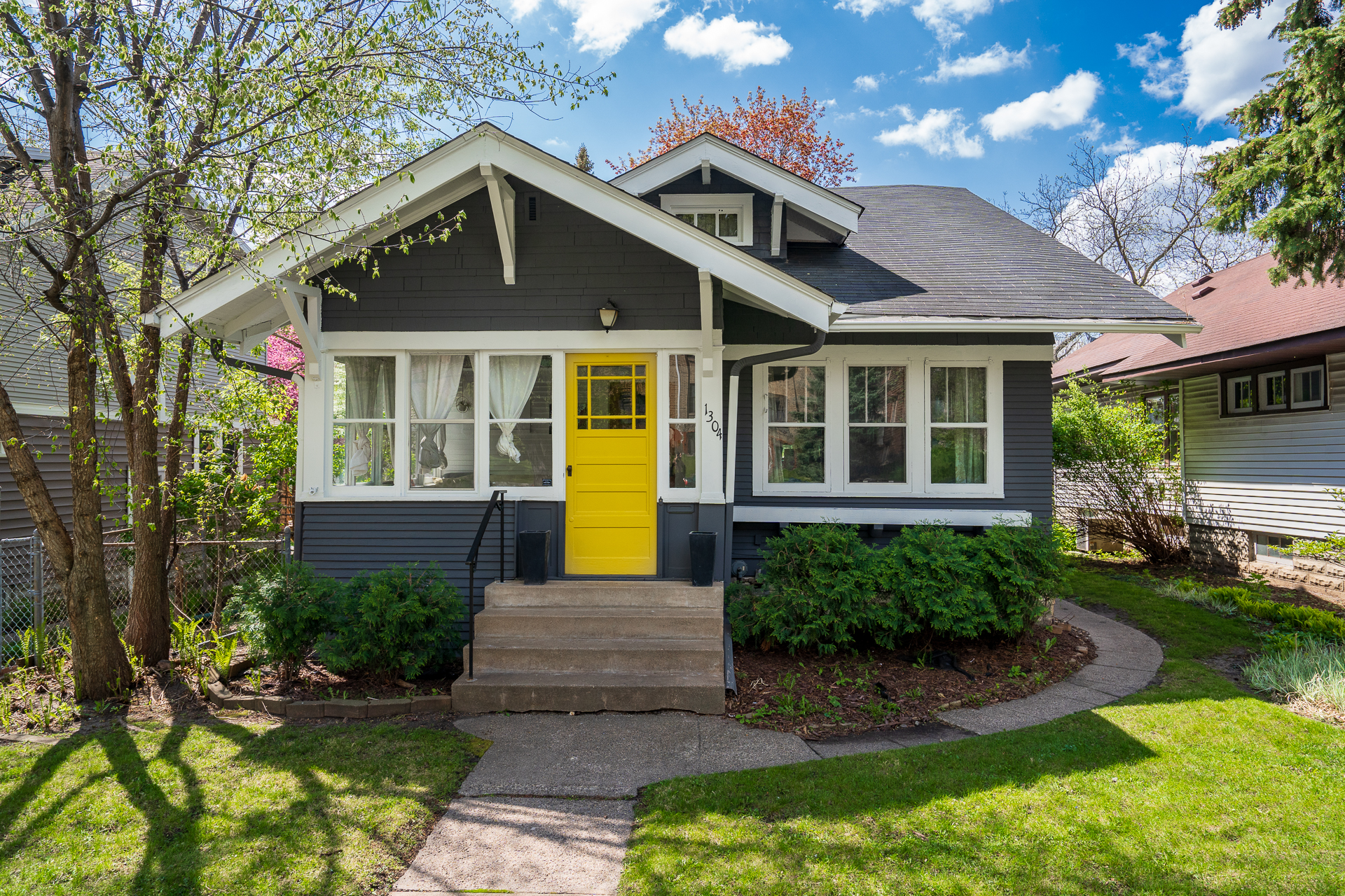 Gray house with a yellow door surrounded by greenery under a blue sky.