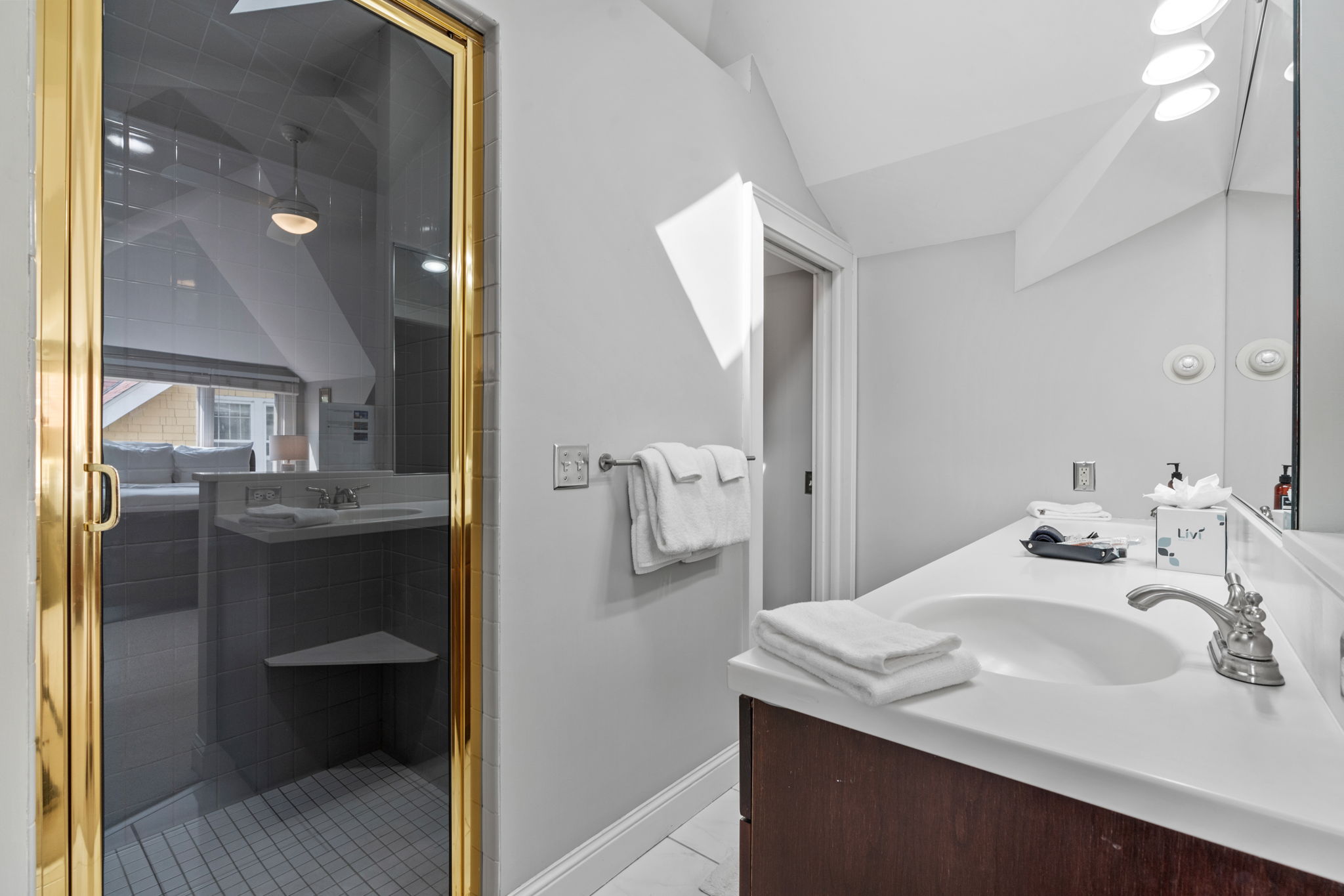 A bright and stylish bathroom with a gold shower door, sleek countertop, and elegant decor.