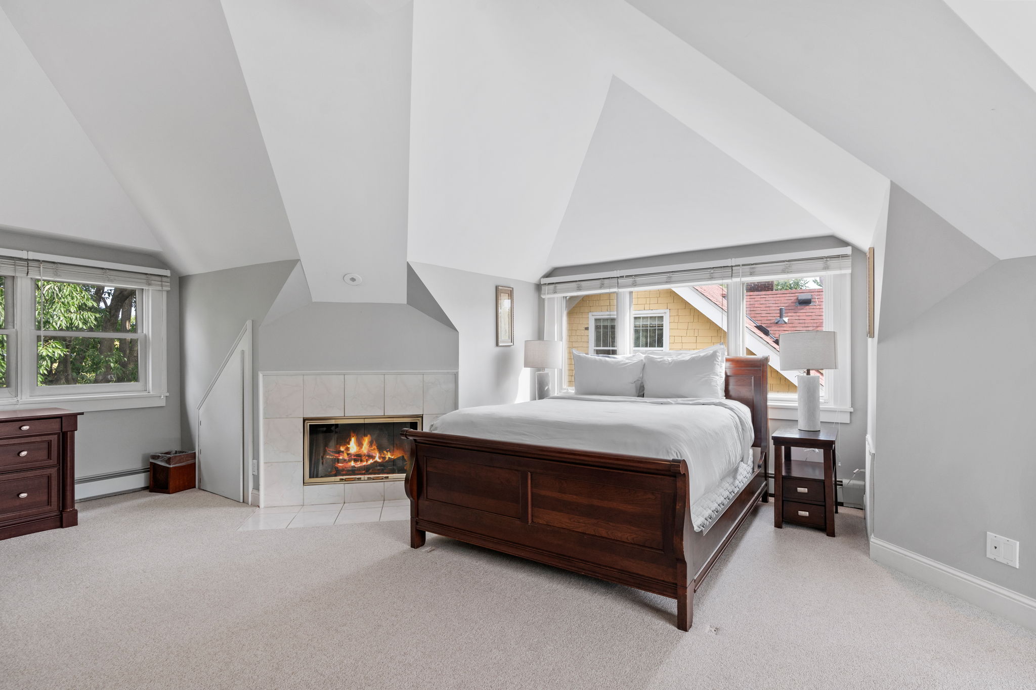 A cozy bedroom featuring a sleigh bed, modern decor, and a warm fireplace.