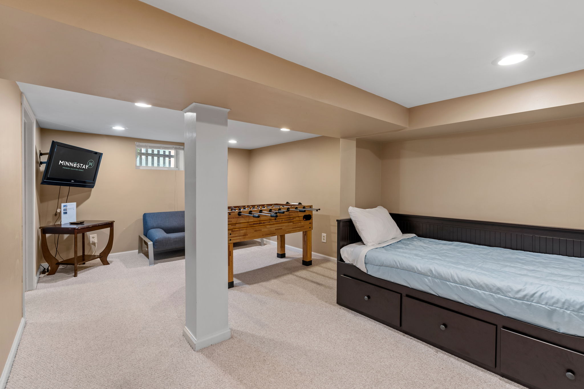 A cozy basement area featuring a foosball table, a TV, and a bed.