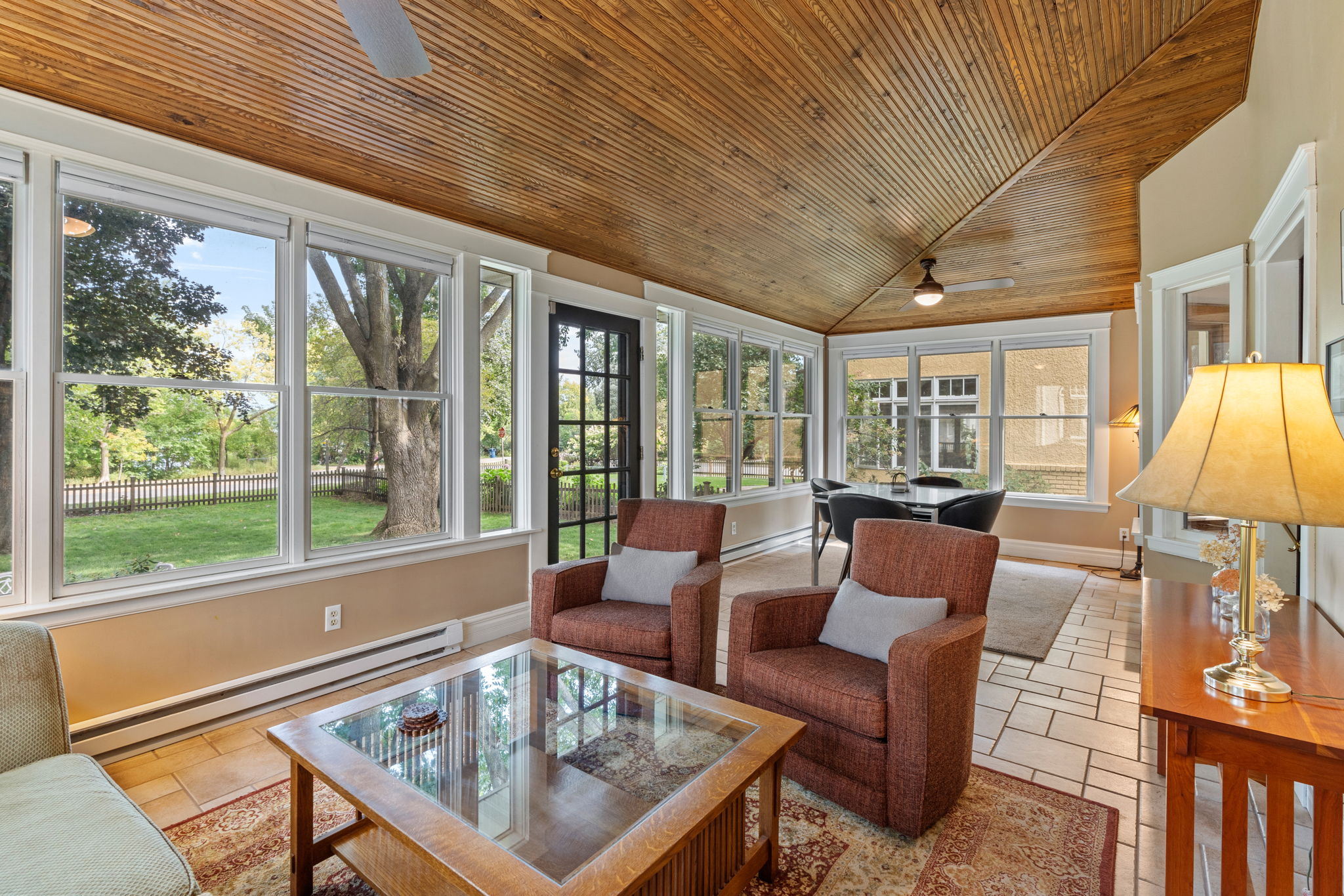 A bright and inviting sunroom with wood-paneled ceiling and comfortable seating.