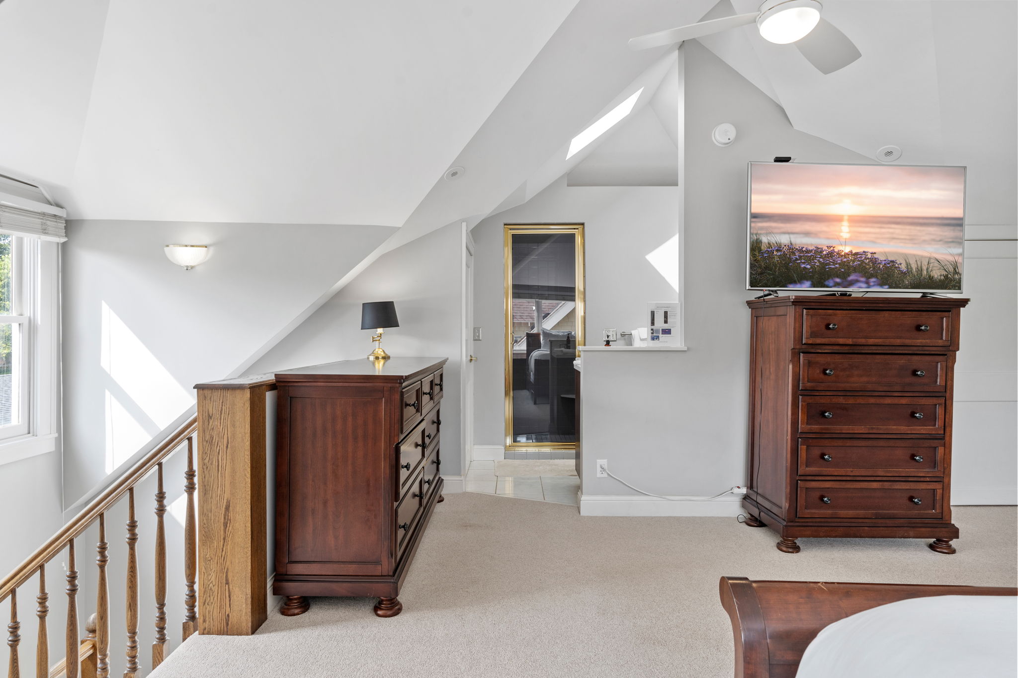 A cozy bedroom corner showcasing a wooden dresser, lamp, and a flat-screen TV displaying a sunset.