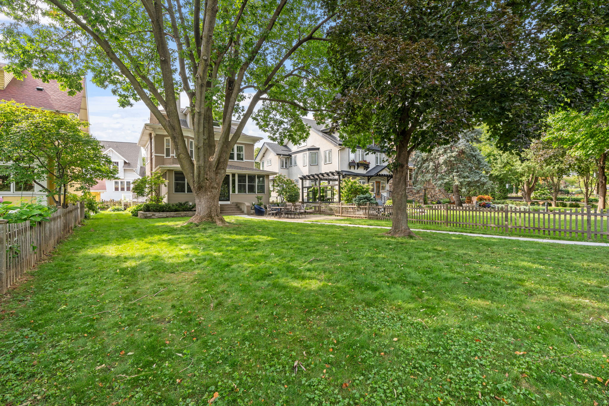 A serene backyard with lush grass and large trees next to charming homes.