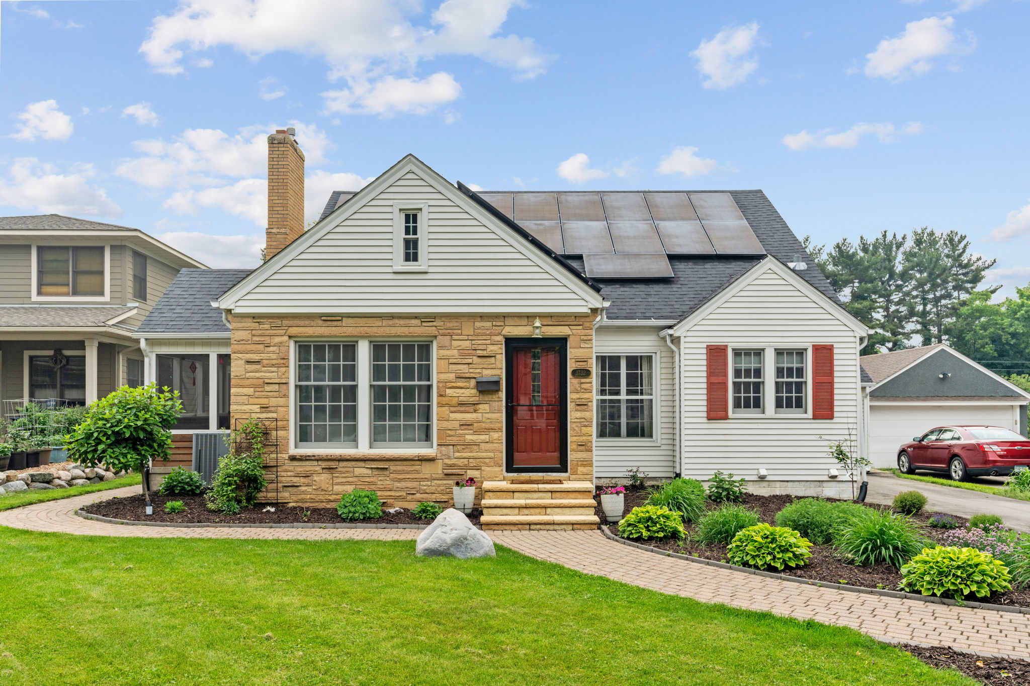 A charming home featuring a blend of stone and siding, complete with solar panels and vibrant landscaping.