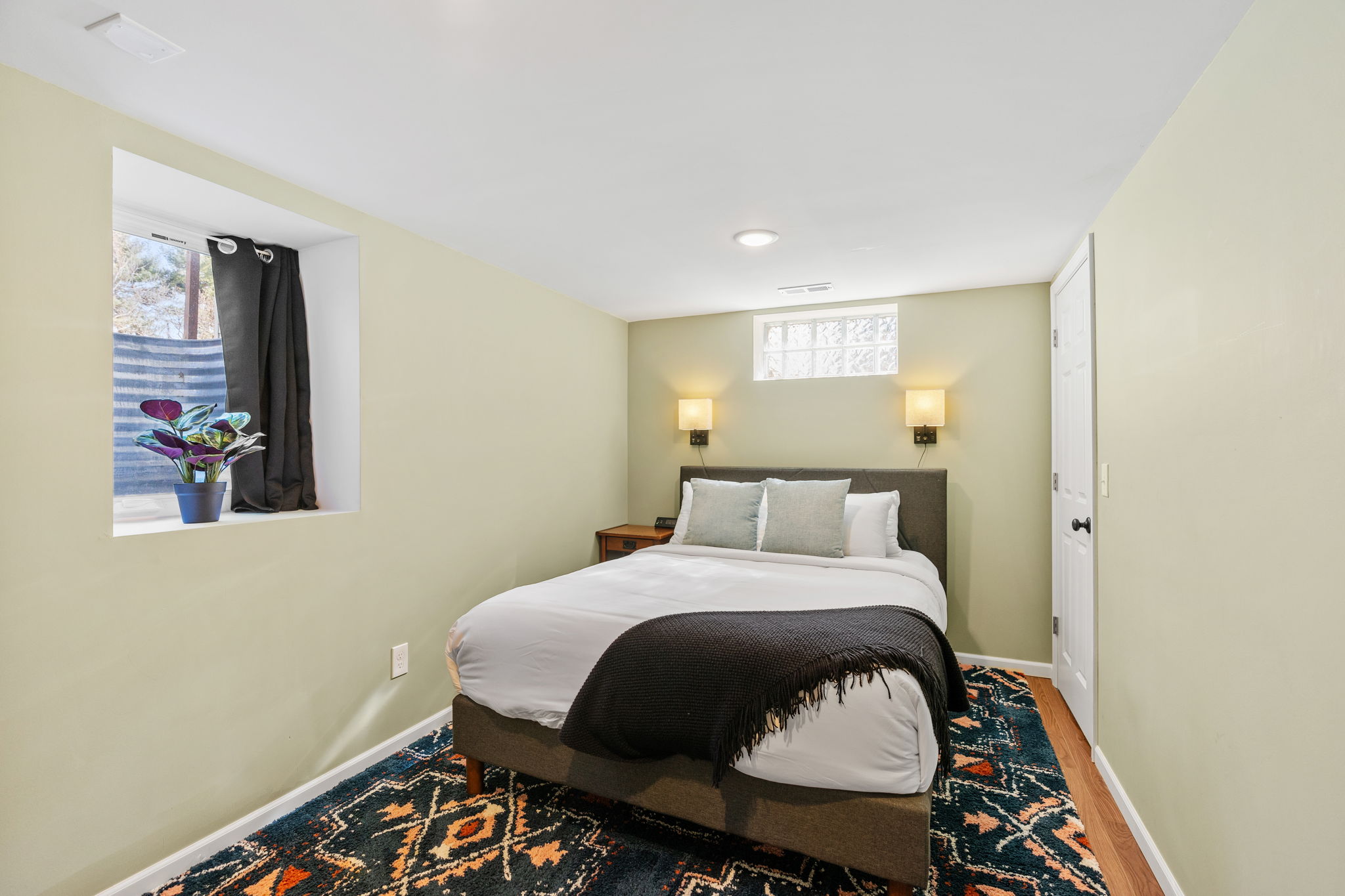 A cozy bedroom featuring a neatly made bed and a potted plant by the window.