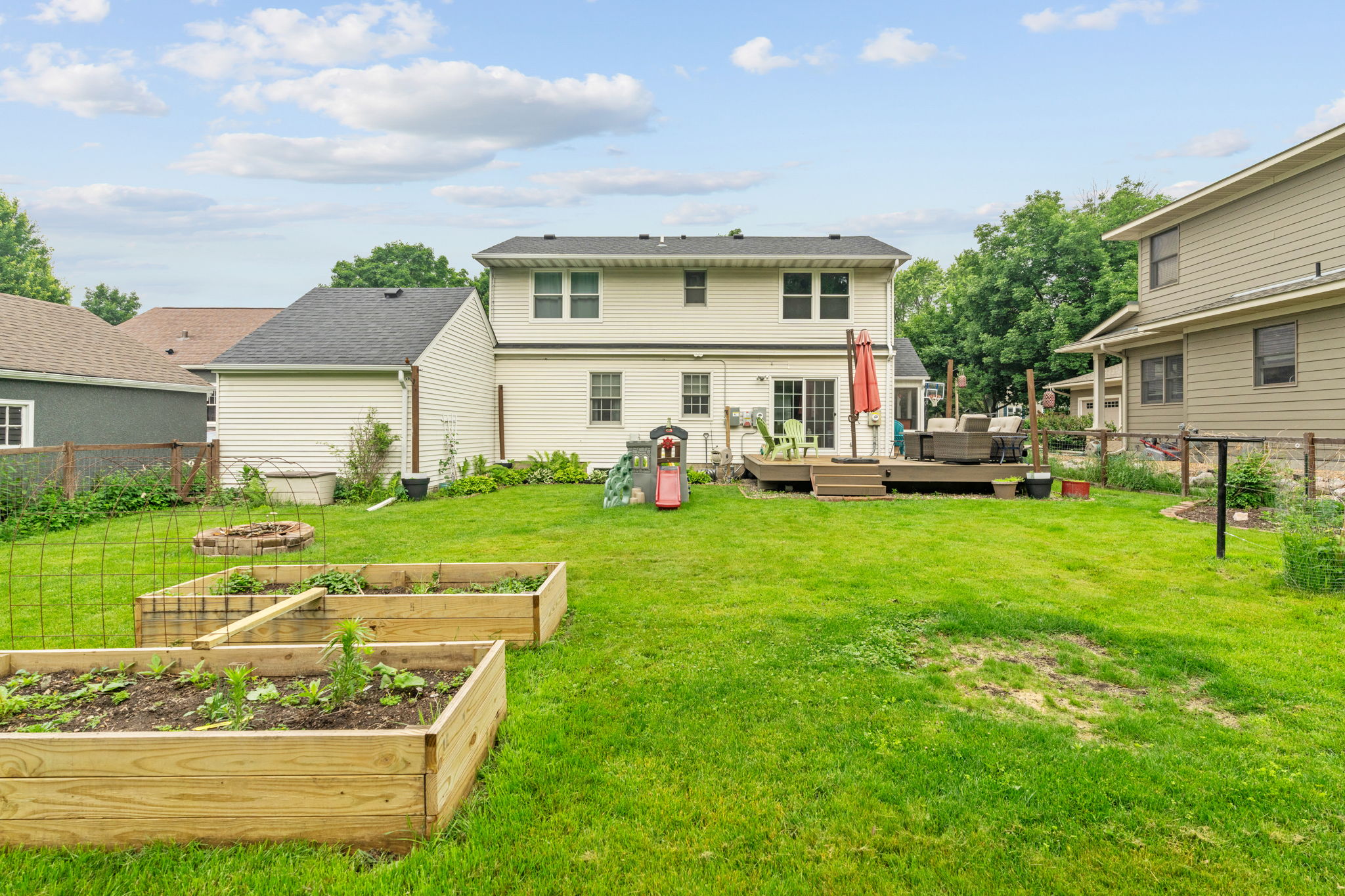 A charming backyard with a spacious lawn, garden beds, and a cozy deck.