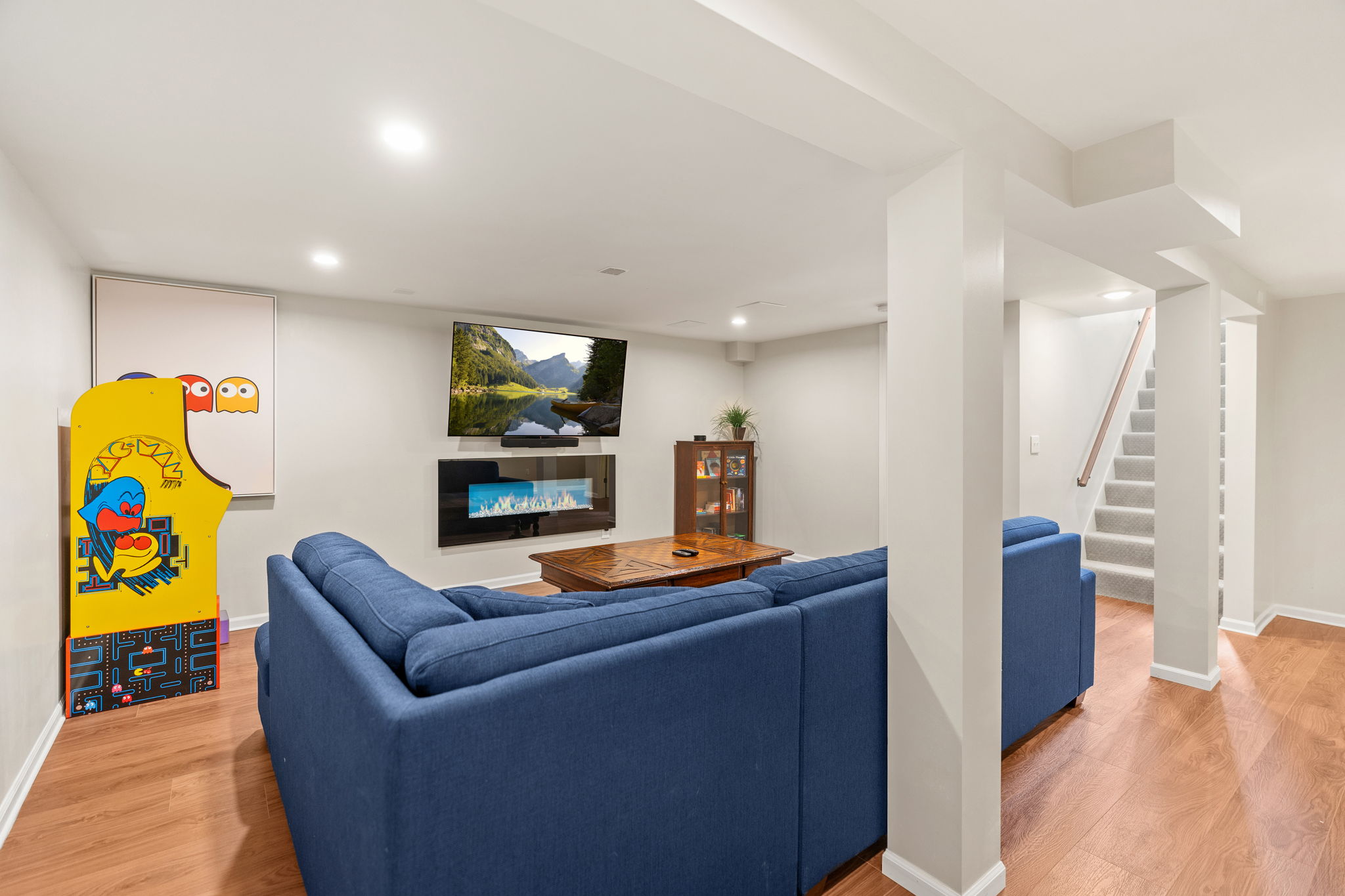 A modern basement recreation room with cozy seating and vintage arcade game.