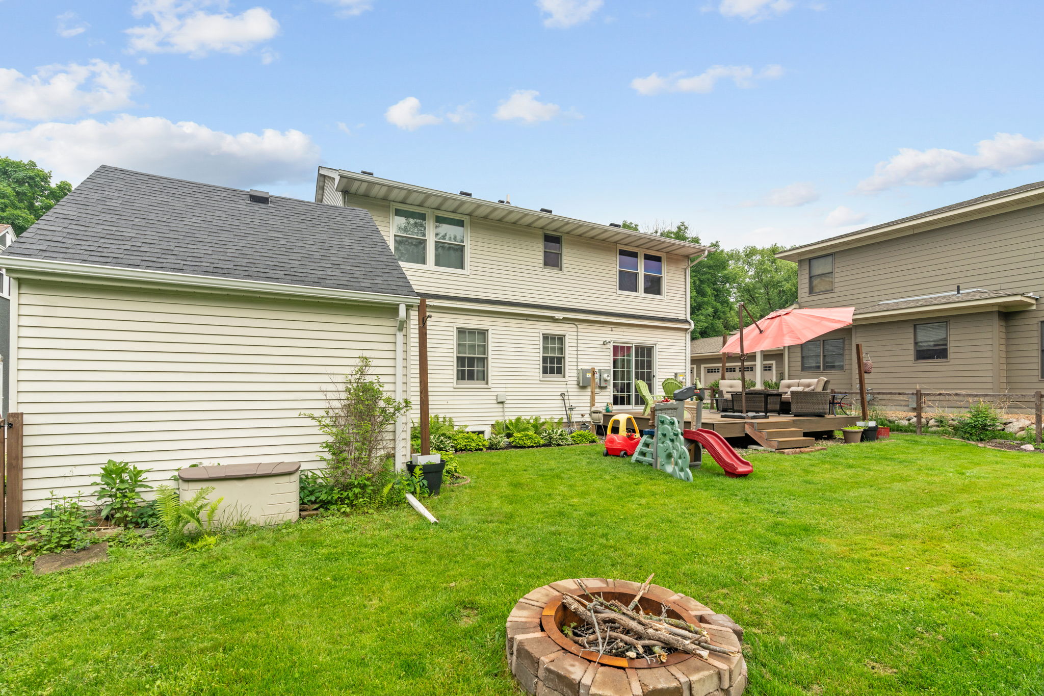 A beautifully maintained suburban backyard featuring a cozy seating area, children's toys, and a fire pit.