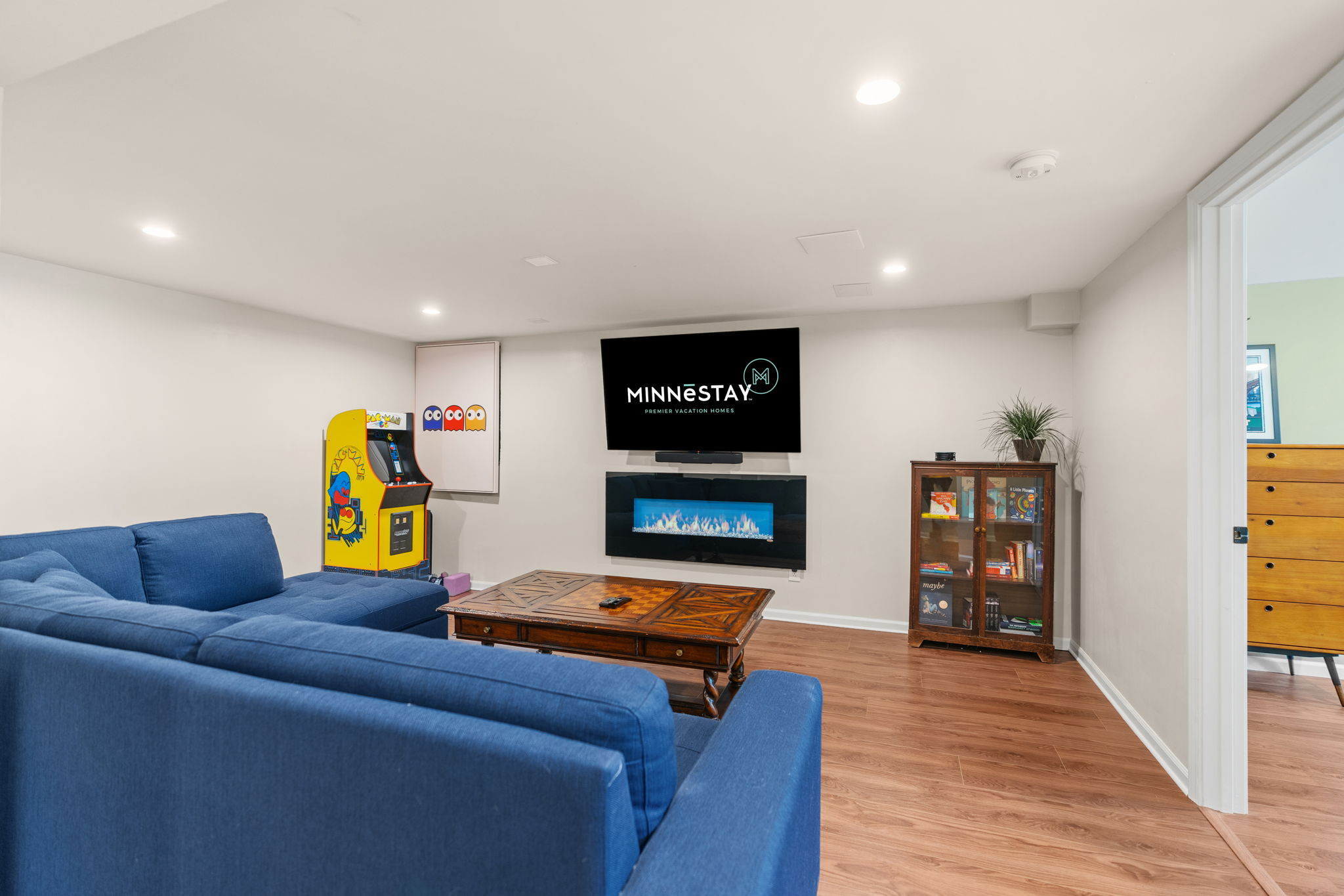A stylish living space featuring a blue sectional sofa, an arcade machine, and modern decor.