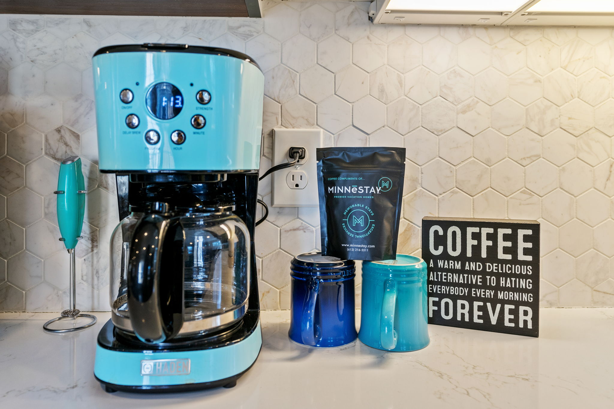 A vibrant coffee station showcasing a turquoise coffee maker and mugs, with a humorous coffee sign.