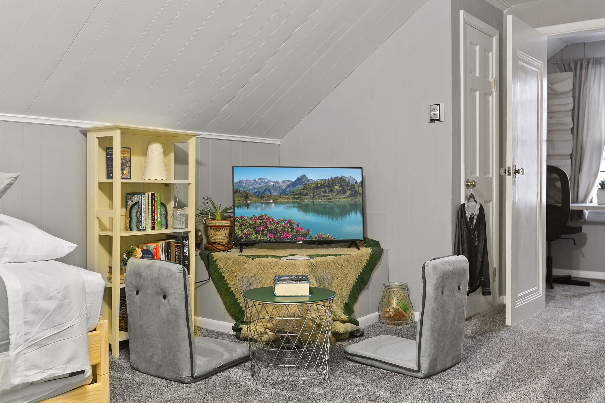 A cozy attic corner with a seating area, books, and a scenic TV display.