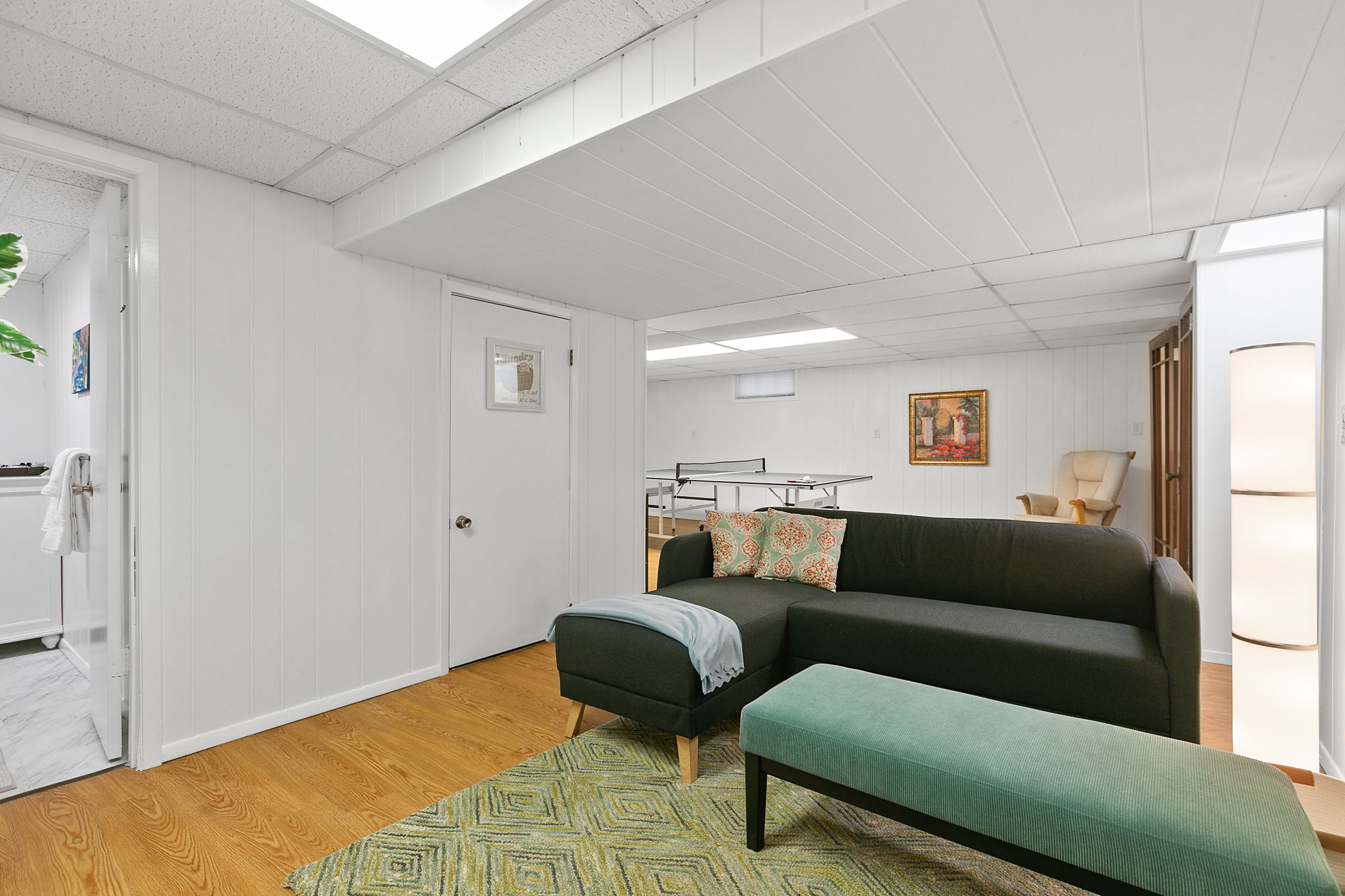 A modern and inviting basement living area with a sectional sofa and ping-pong table.