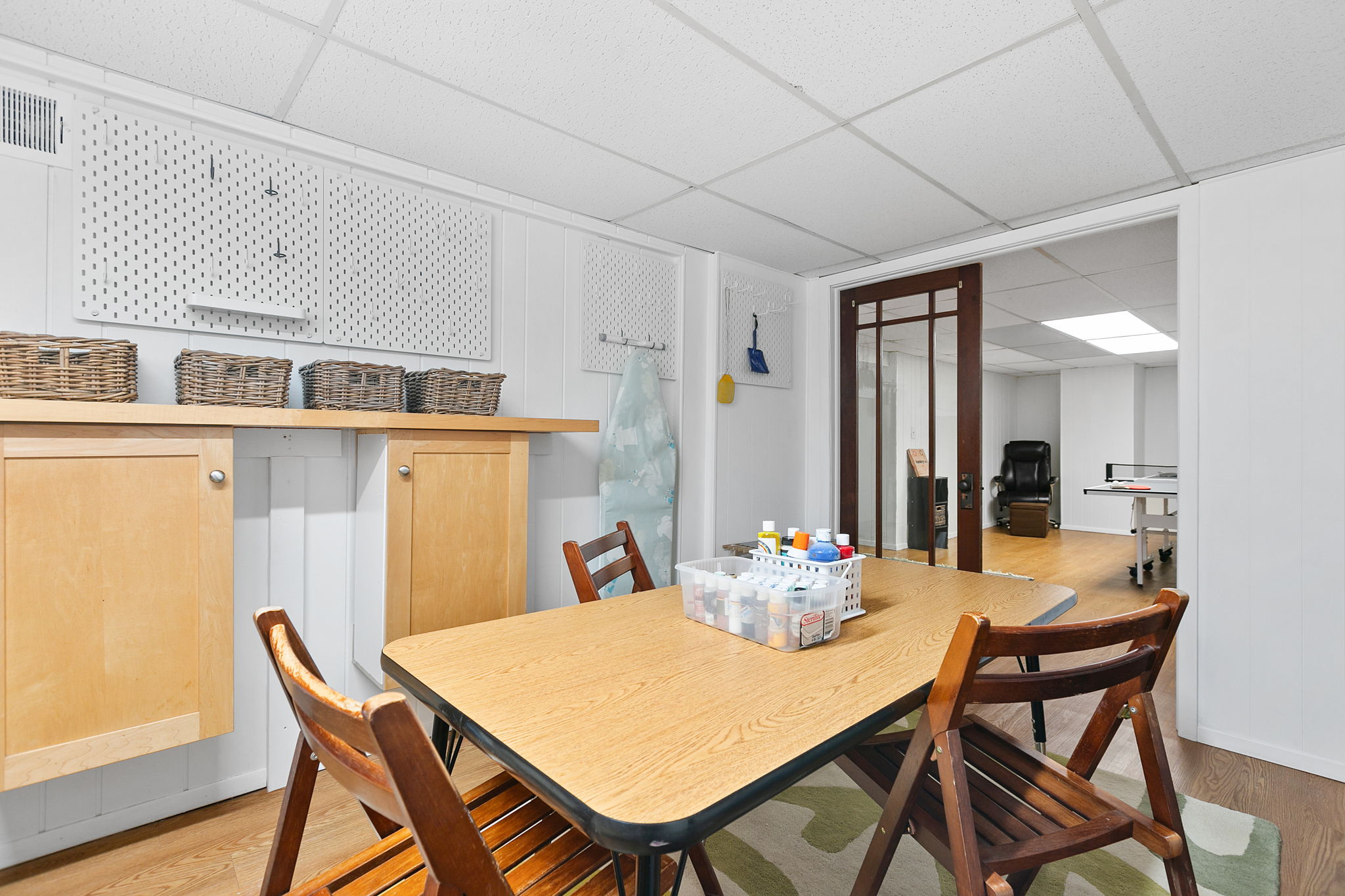 A bright and functional craft area in a basement featuring a wooden table and storage solutions.