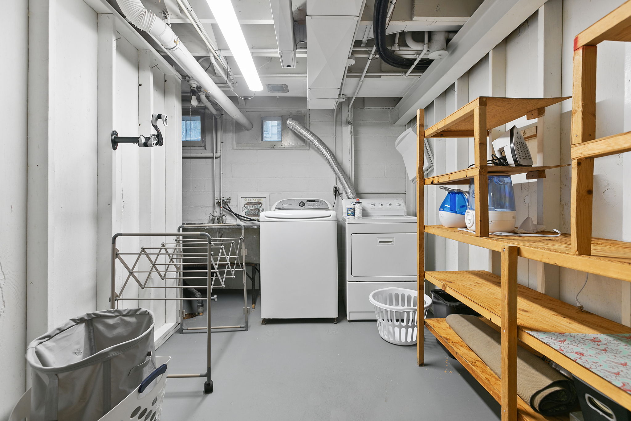 A well-organized basement laundry room featuring a washing machine, dryer, and storage shelves.