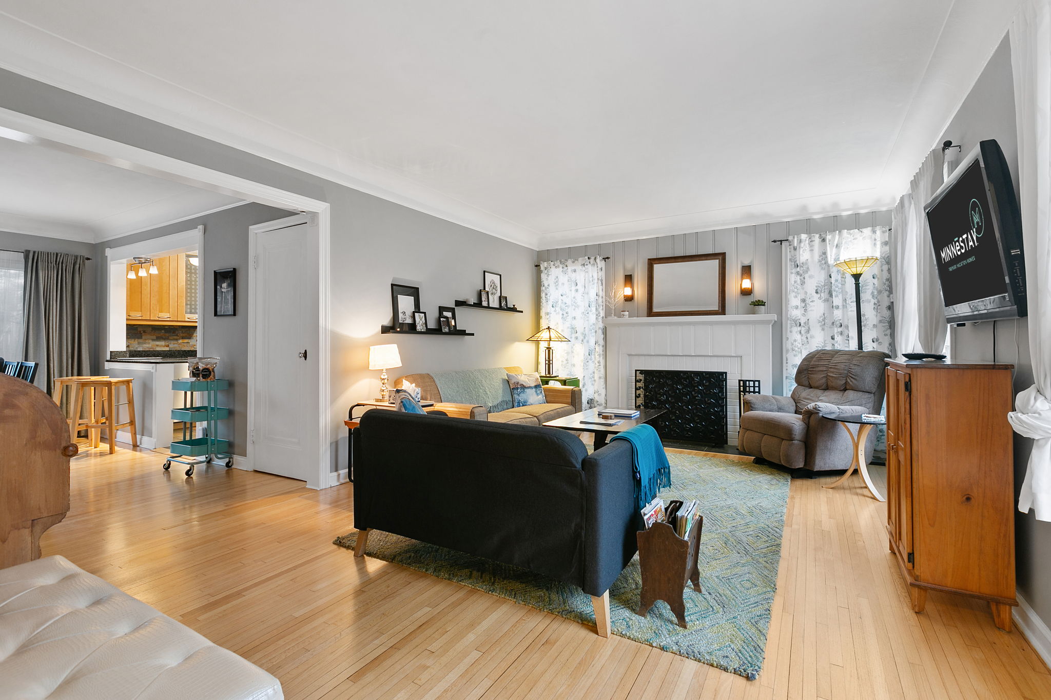 Living room with hardwood flooring, a black couch, a fireplace, and a view of the kitchen.