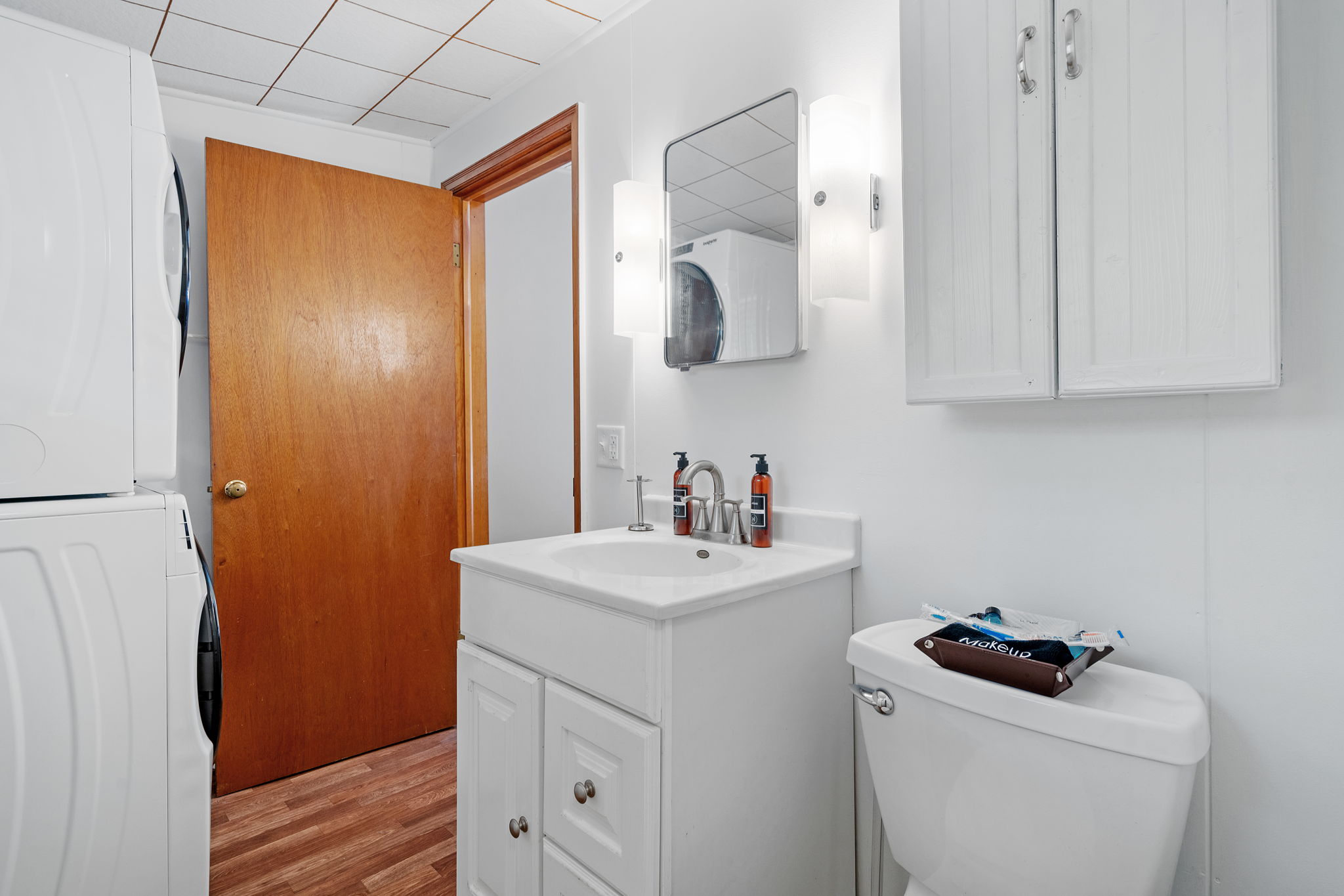 A compact bathroom featuring a modern vanity, laundry appliances, and tasteful lighting.