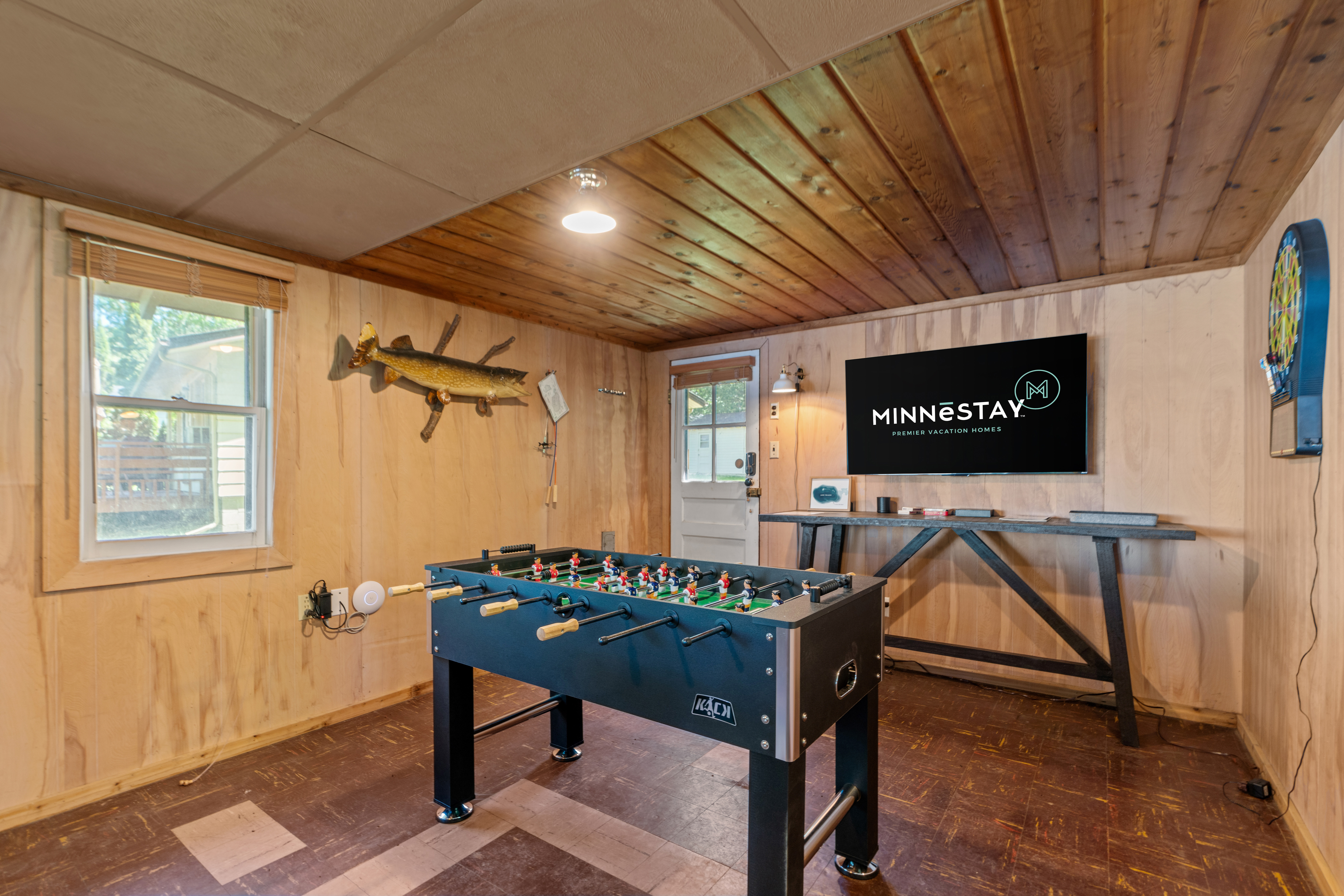 A cozy game room featuring a foosball table, a mounted fish, and a television with a vacation rental logo.