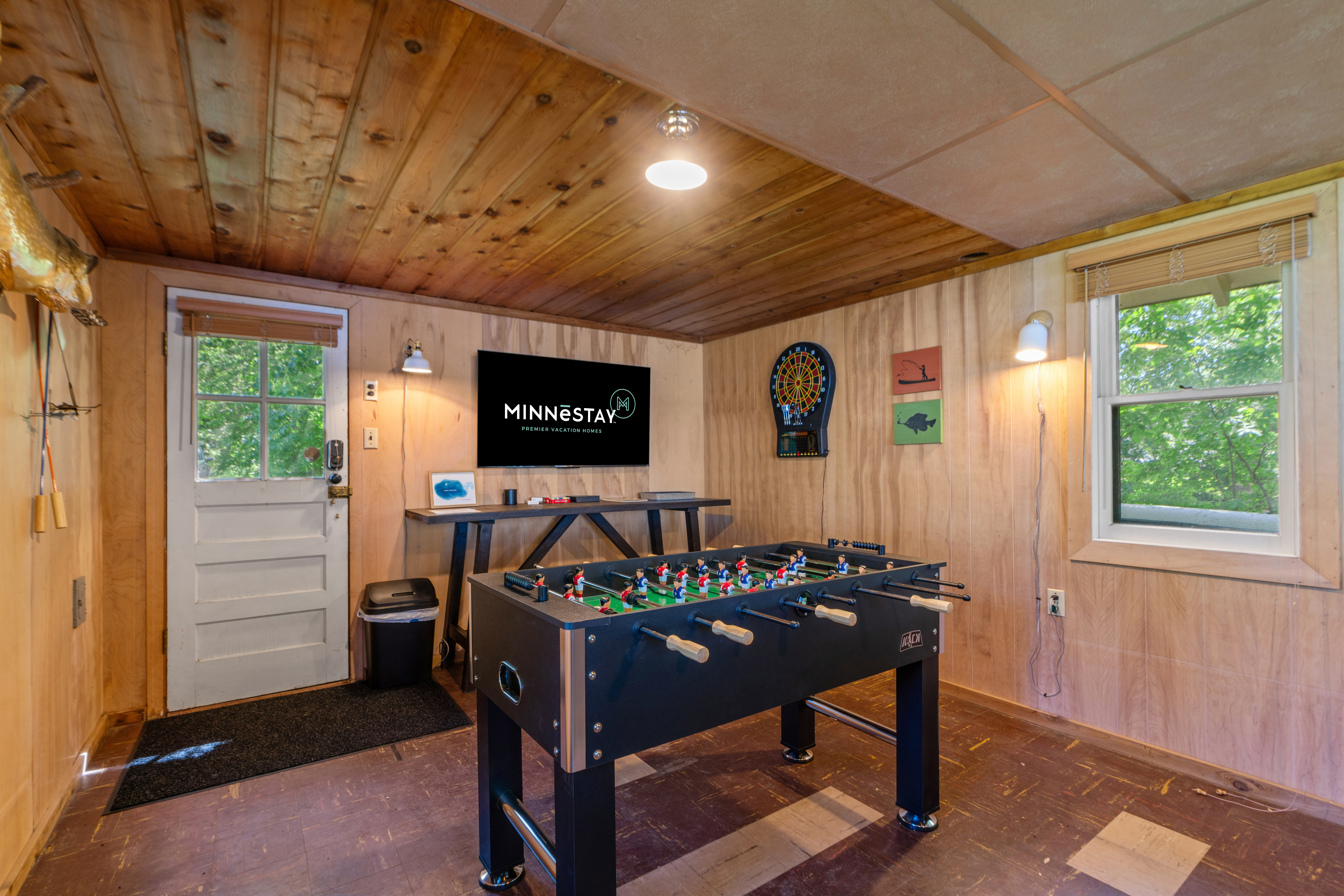 A cozy recreational room featuring a foosball table, TV, dartboard, and natural light from a window.