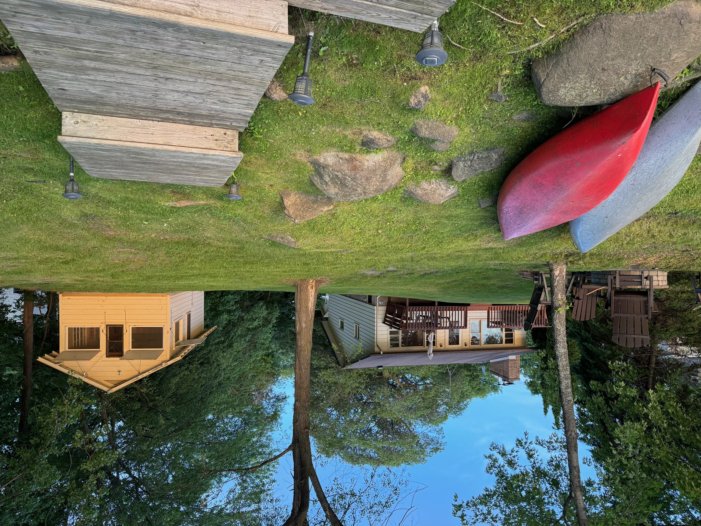 A scenic lakeside cabin with kayaks, inviting deck, and lush surrounding greenery.