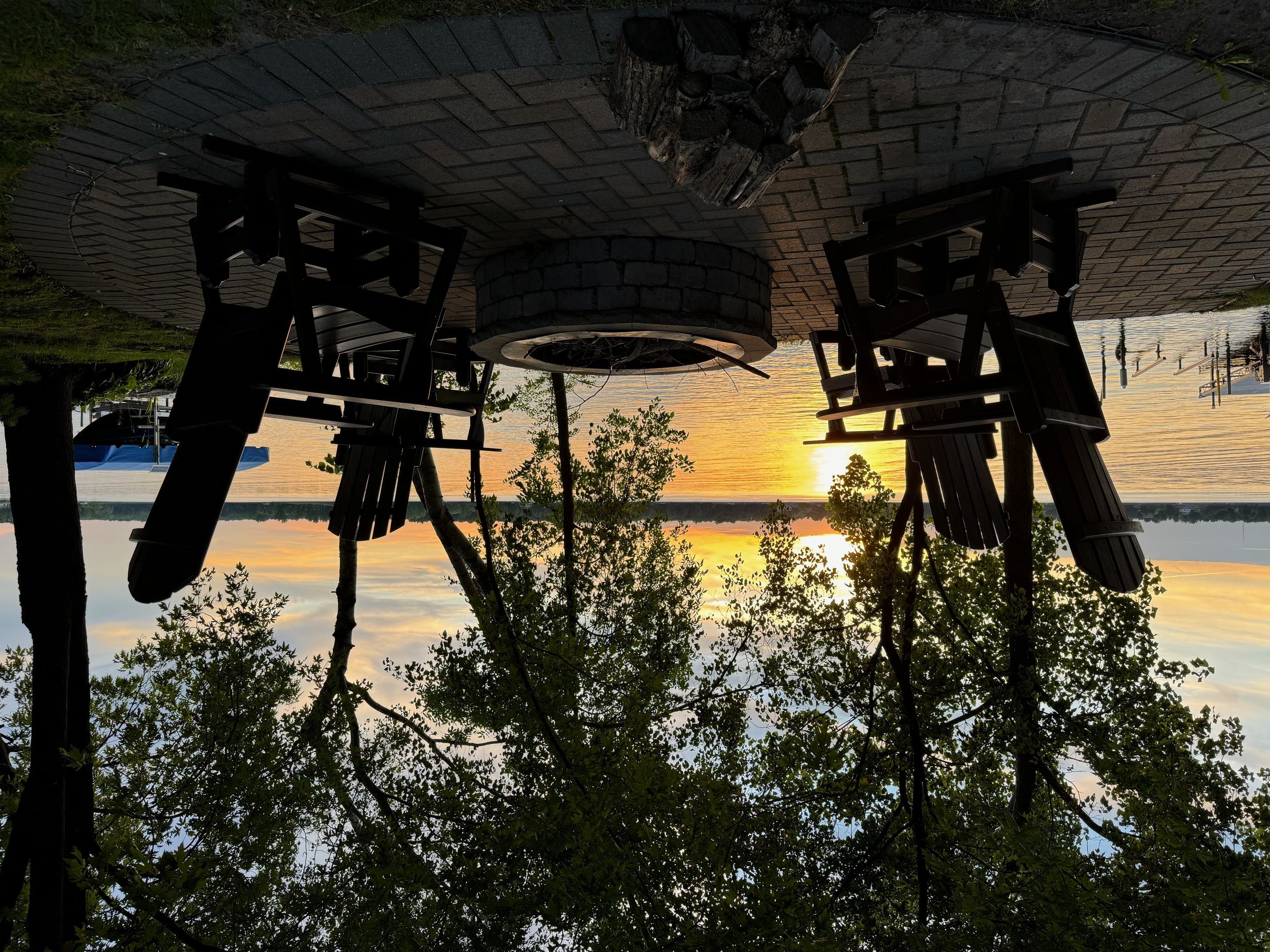 A serene lakeside sunset with adirondack chairs around a fire pit.